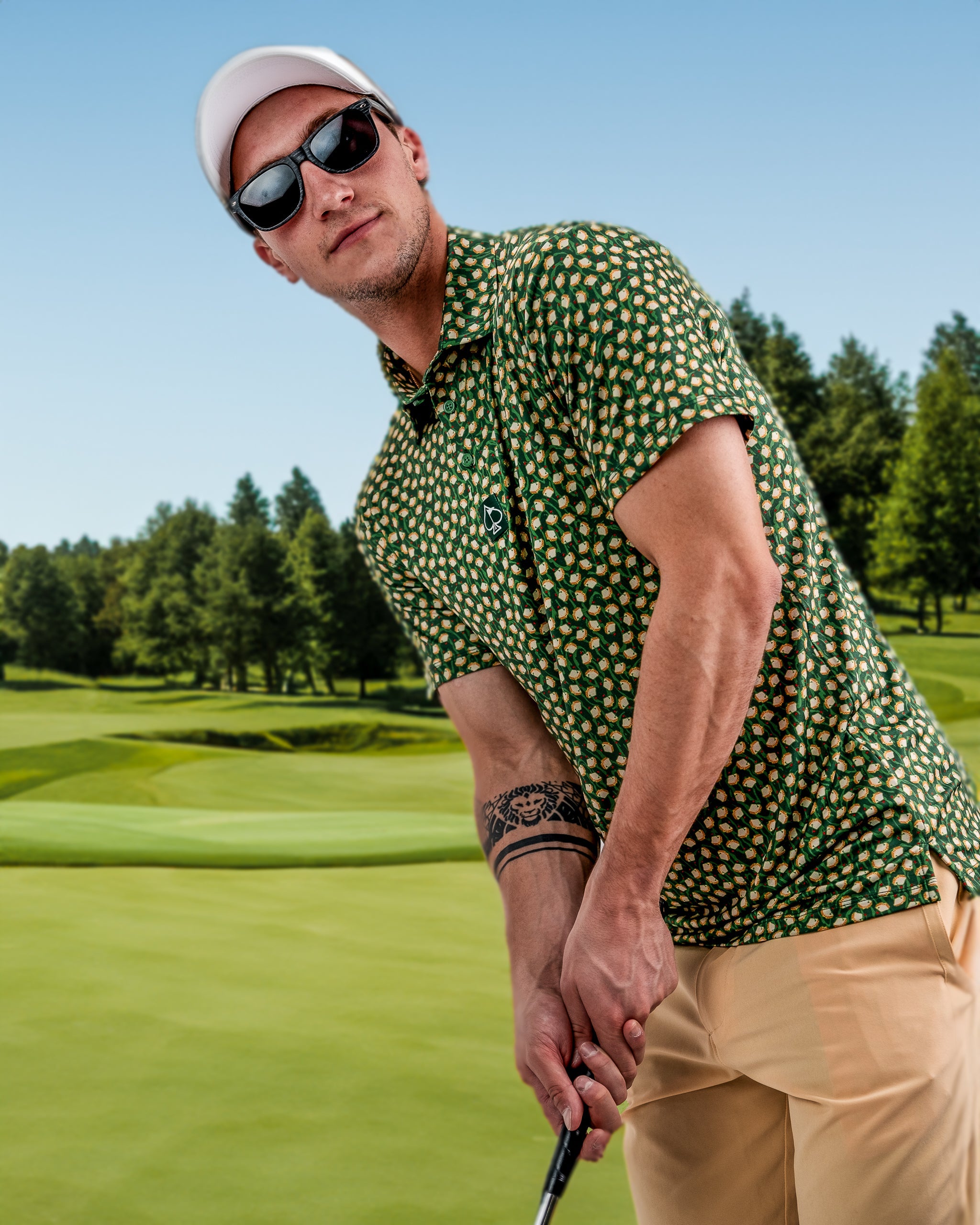 Man in bold green golf shirt with colorful pattern, beige pants, white cap, and sunglasses on a golf course.