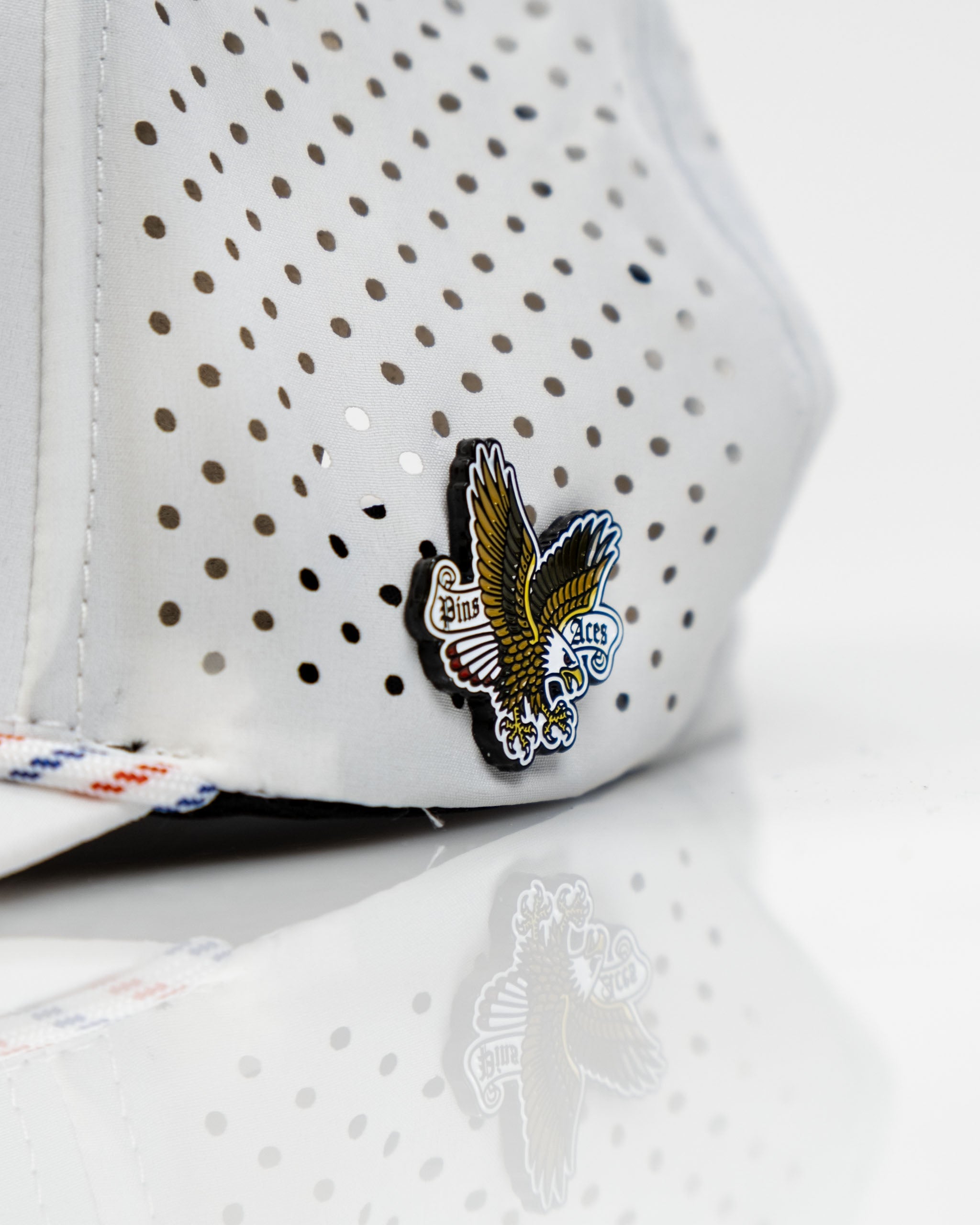 Perforated white rope hat featuring a Freedom Eagle design and Pins and Aces logo for stylish golf wear.
