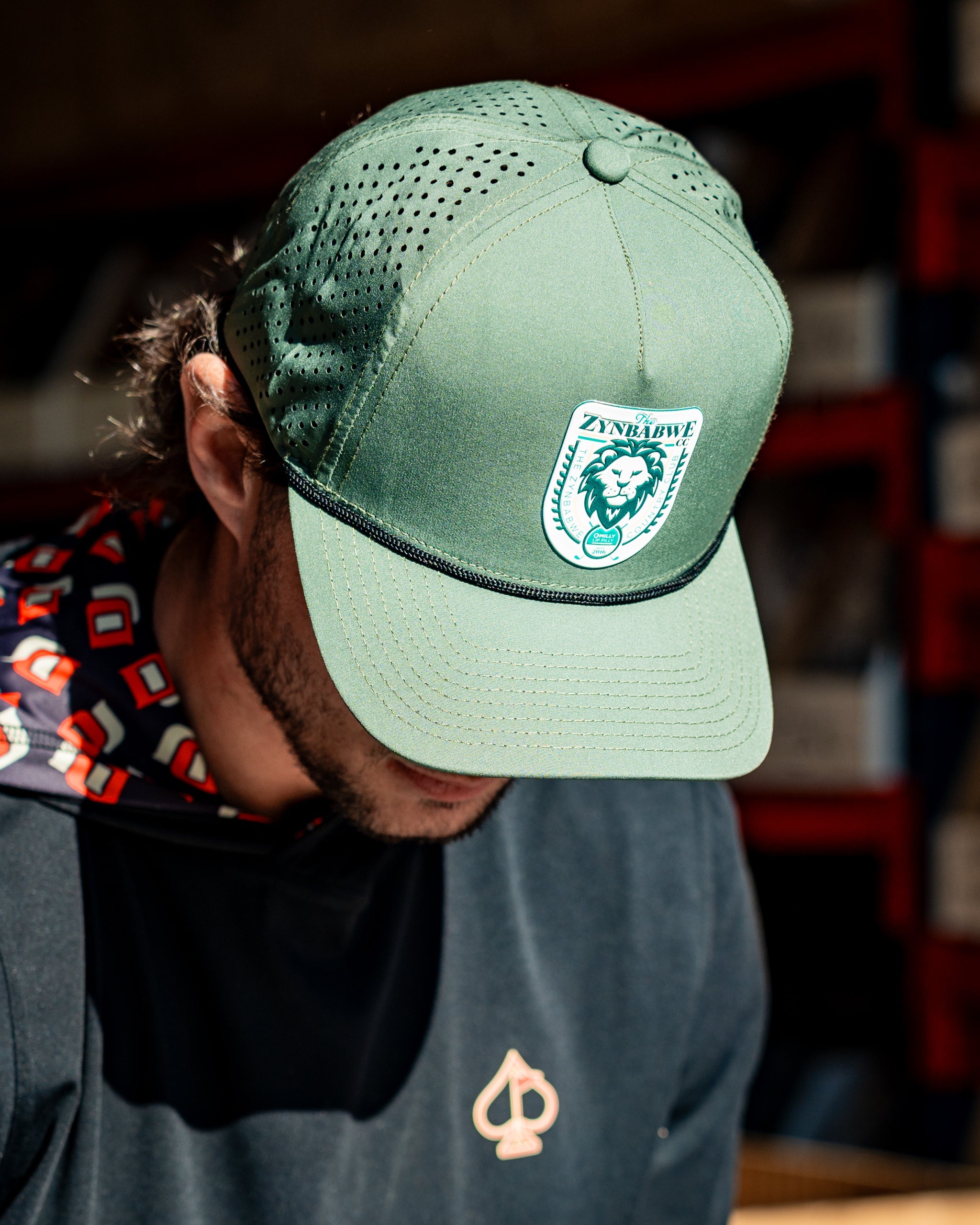 Perforated olive rope hat featuring Zynbabwe Country Club branding.