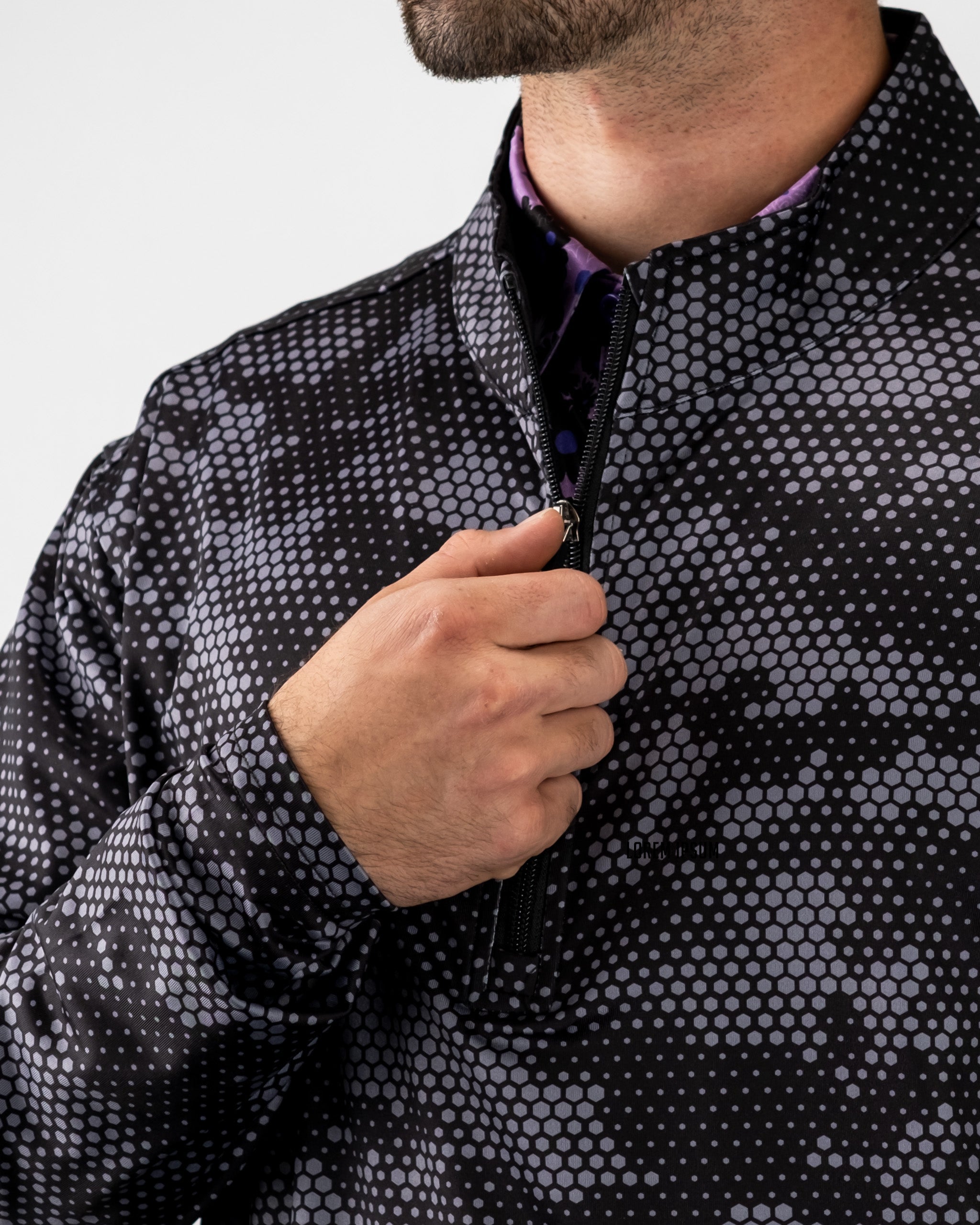 Close-up of a man wearing a black hexagonal pattern Digi Pullover, partially unzipped, with a purple shirt underneath.