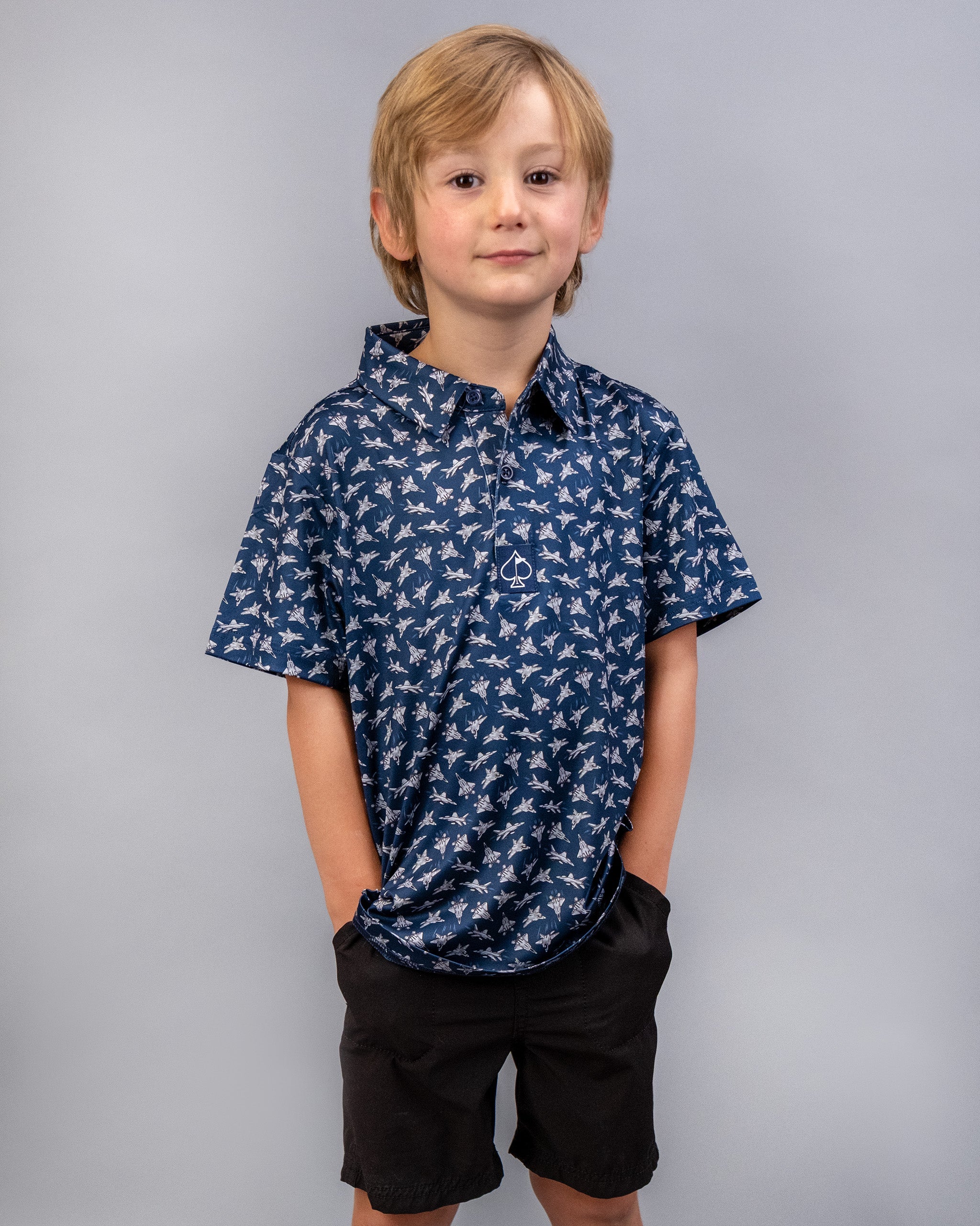 Young boy wearing a navy blue shirt with a white bird pattern and black shorts, standing against a plain gray background.