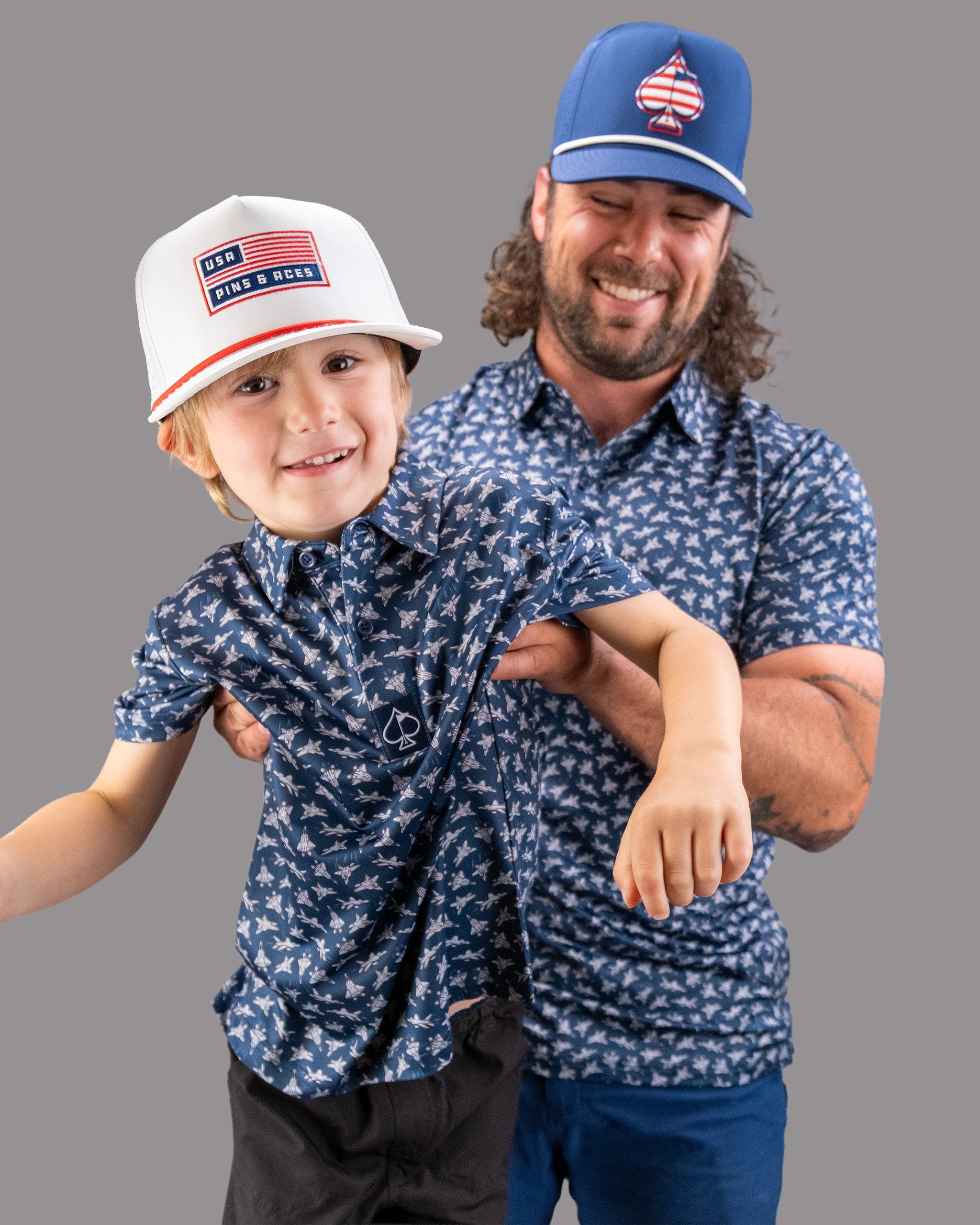A smiling man and boy wearing matching blue shirts and hats featuring patriotic and aviation-inspired designs, promoting Birds of Steel.