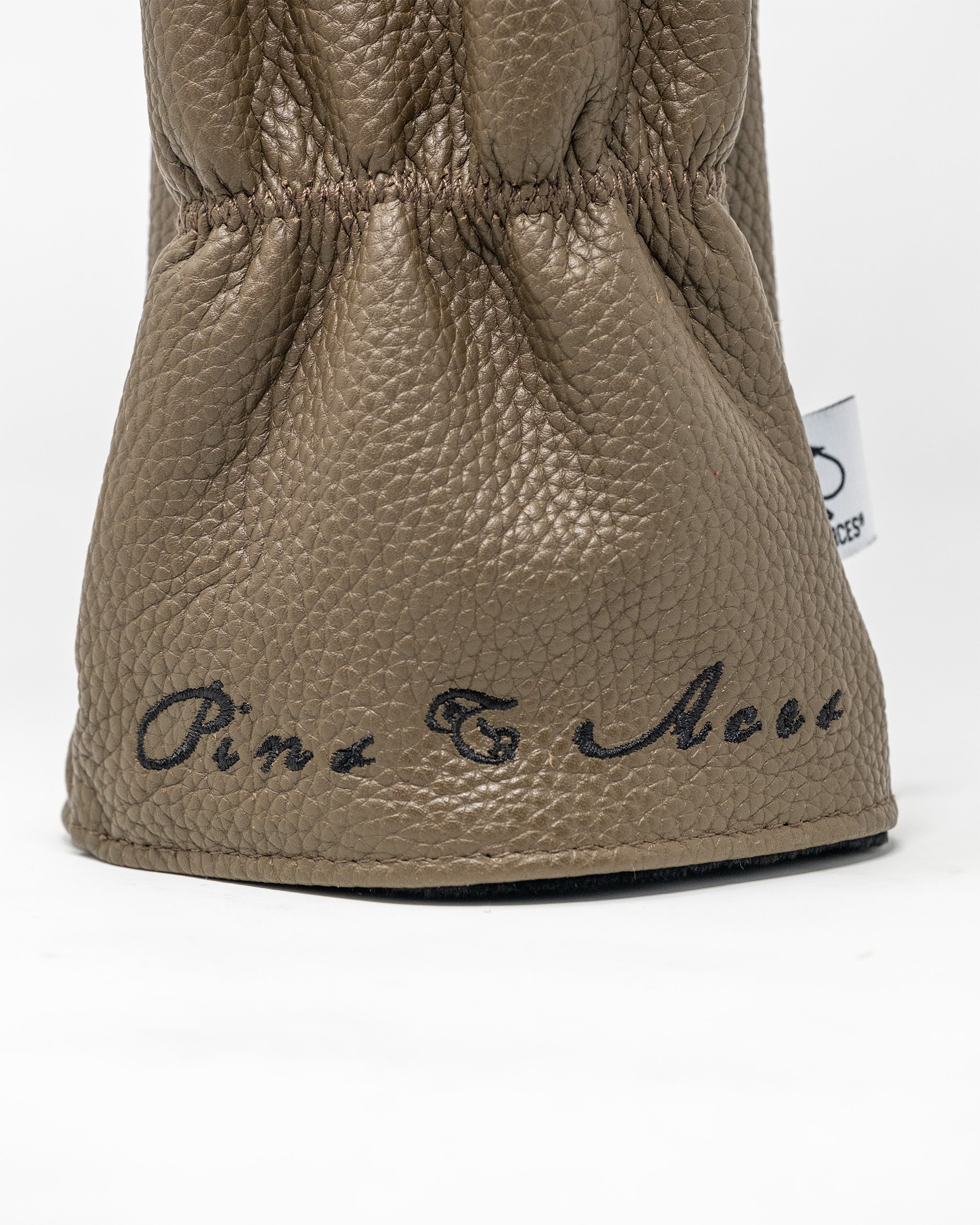 Close-up of a tan textured driver cover with black embroidered text reading "Pins & Aces" at the bottom.