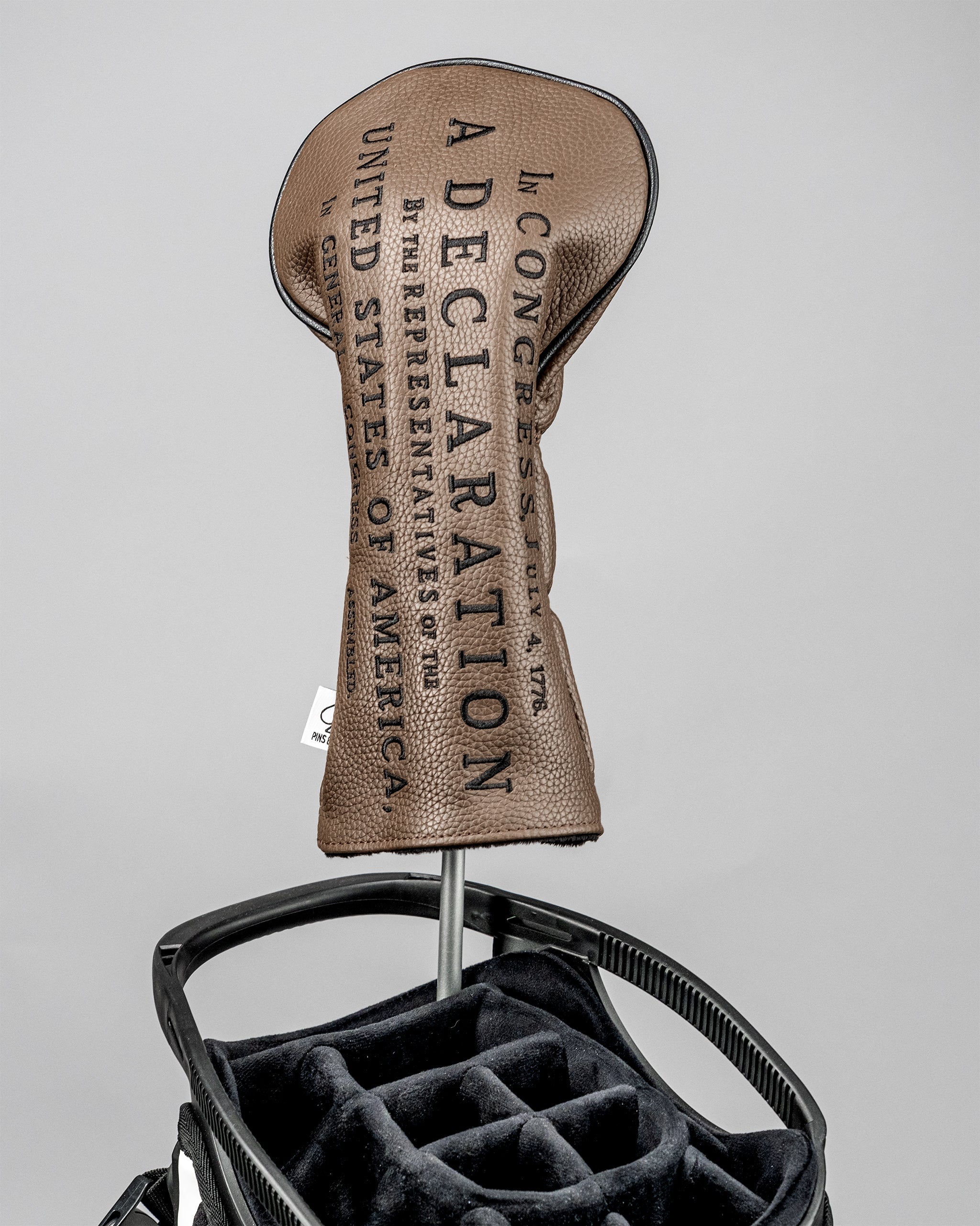 Golf driver headcover with "Declaration" branding, attached to a golf club in a black golf bag with padded compartments.