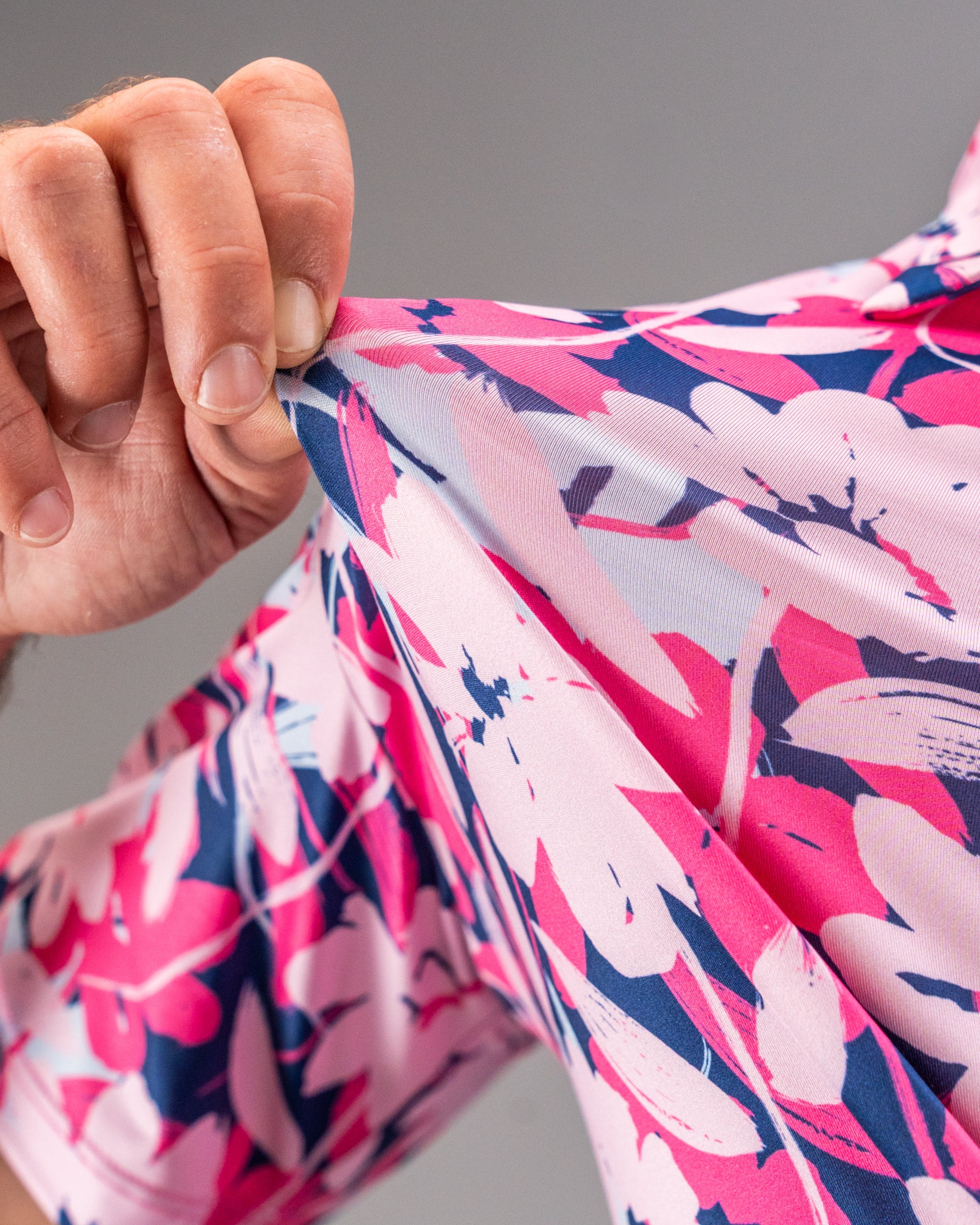 Close-up of pink, white, and navy floral golf apparel fabric being held, showcasing bold, colorful print for standout golf...