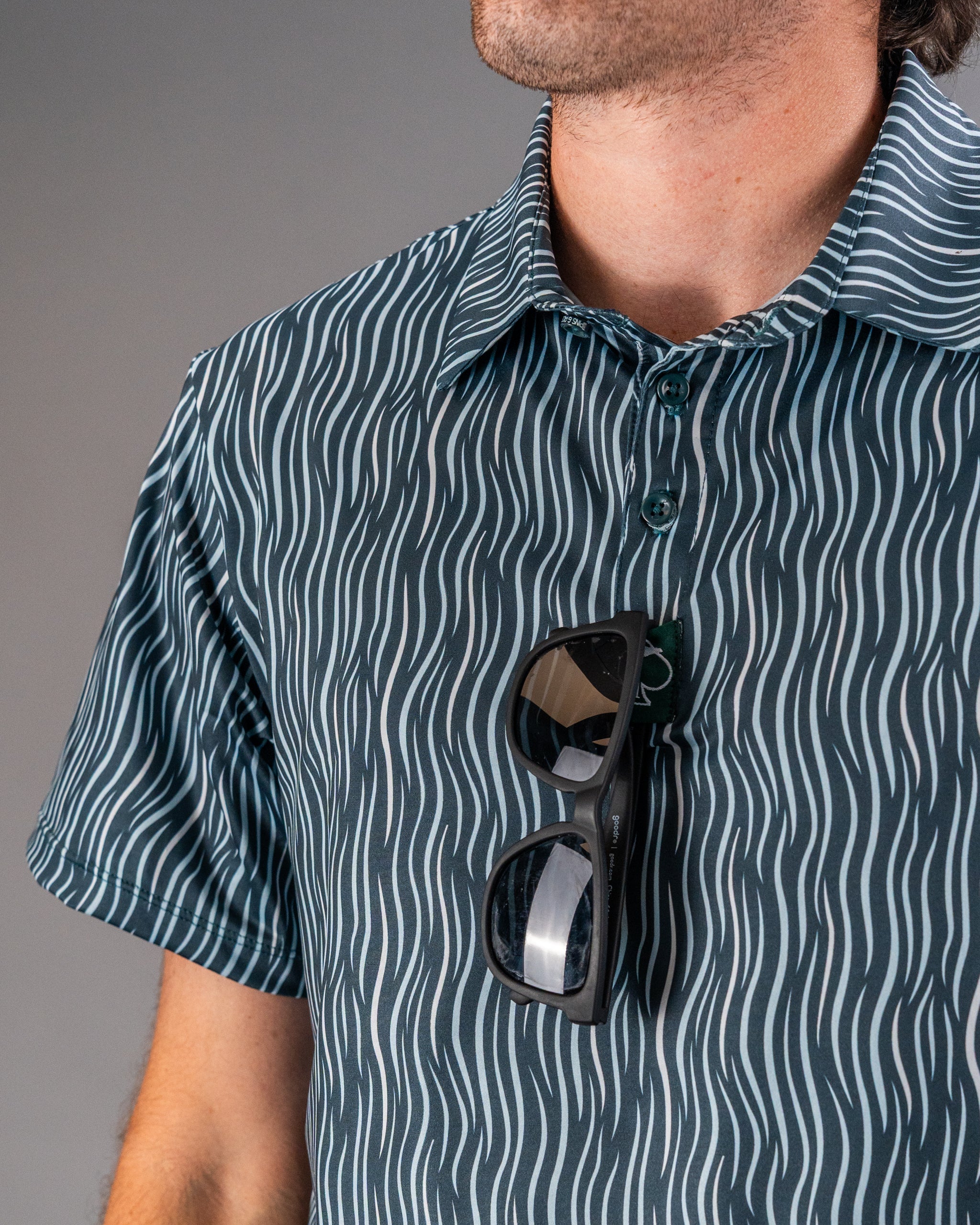 Close-up of a man wearing a bold, patterned golf shirt with sunglasses clipped to the front, highlighting unique golf appa...