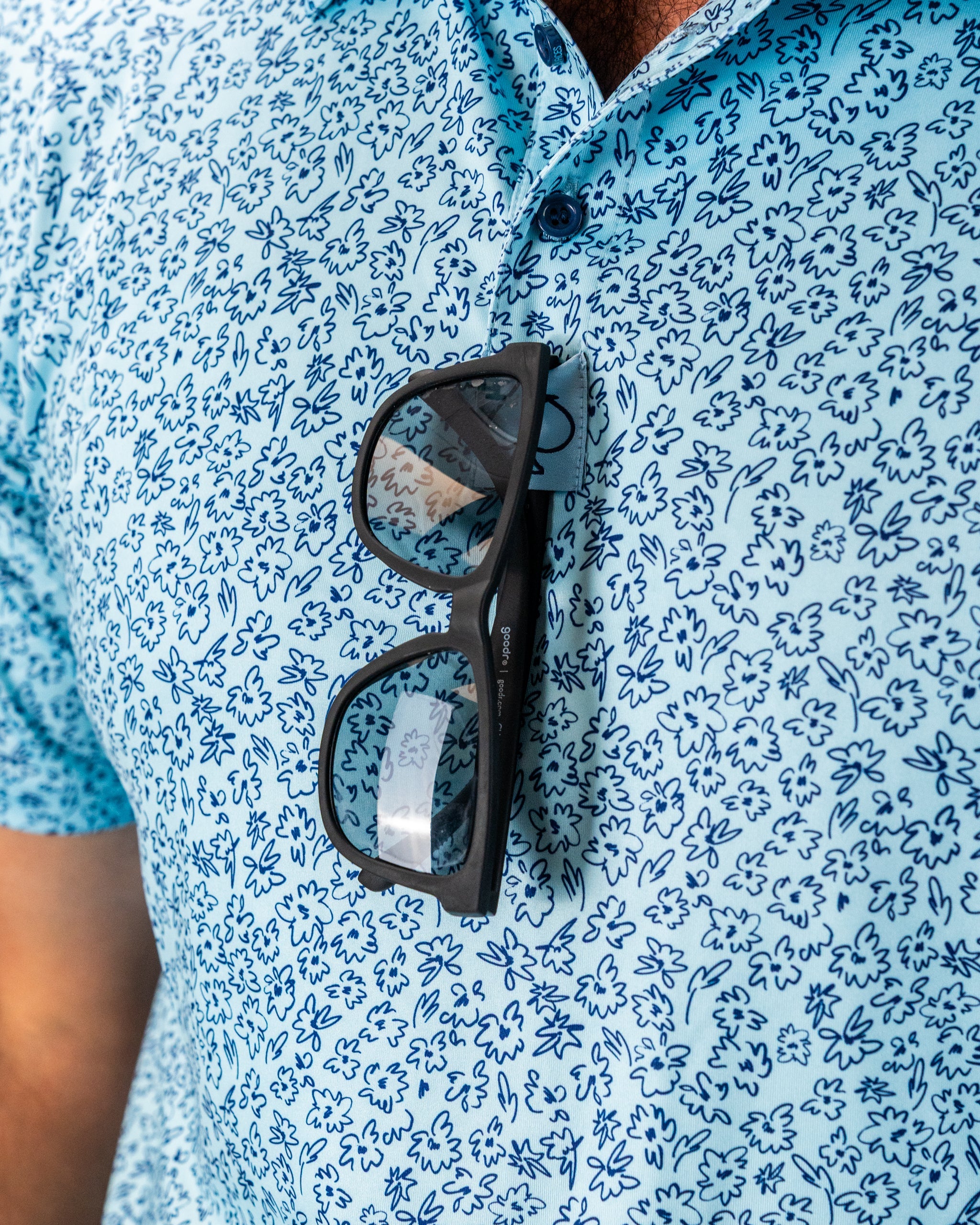 Blue floral patterned shirt with sunglasses resting on the chest, showcasing a stylish and relaxed golf look.
