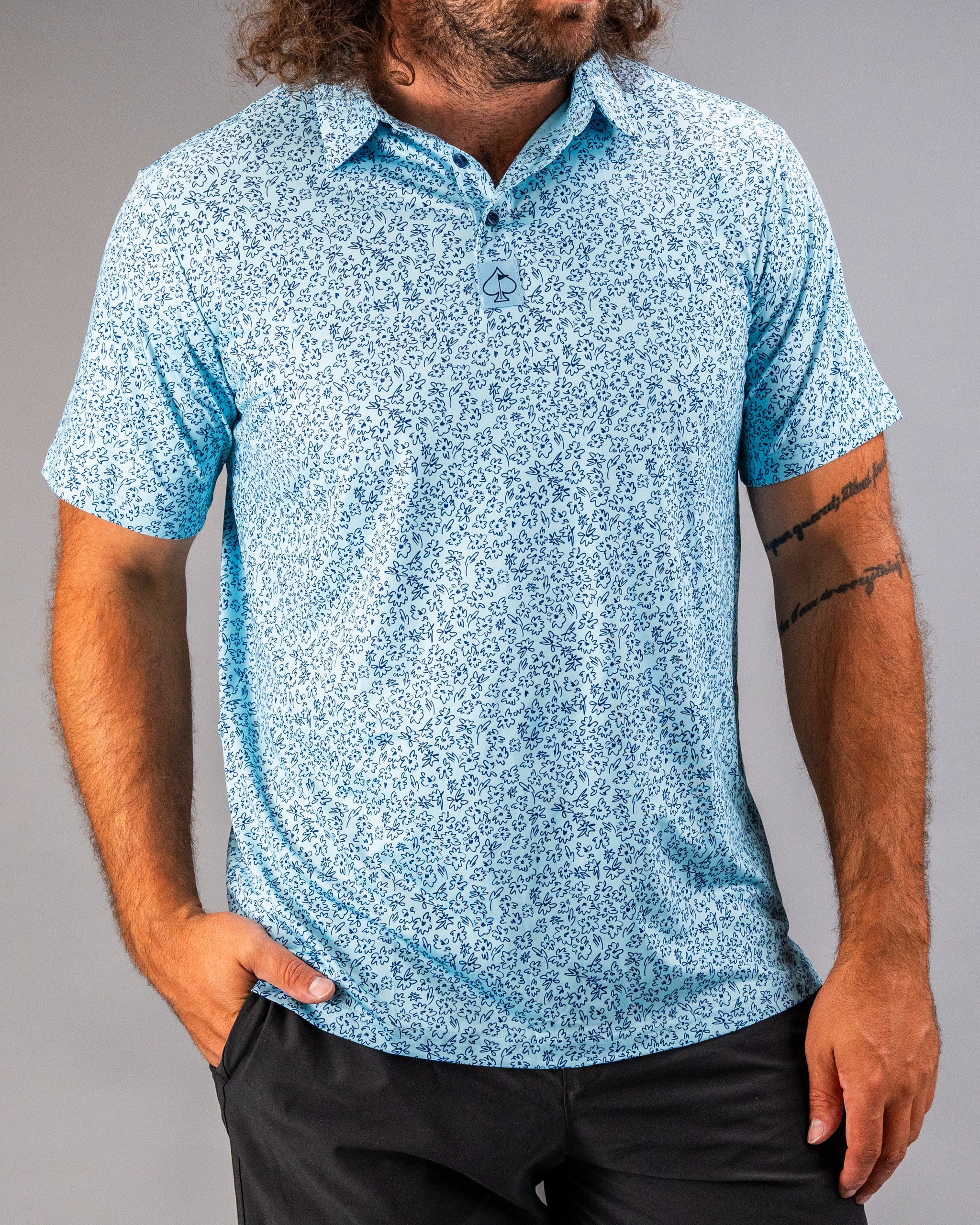 Men's short-sleeve golf shirt in light blue with a floral doodle pattern, featuring a collar and button placket.