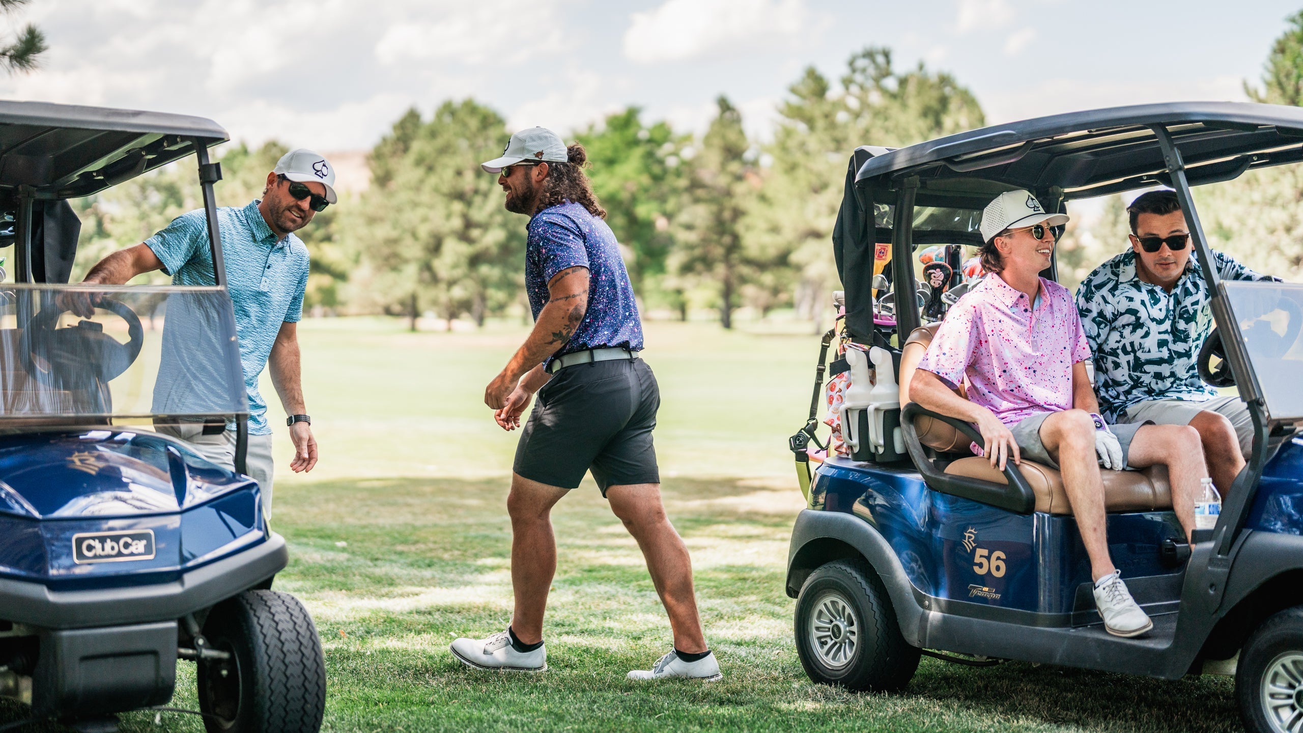 Men in colorful golf apparel socialize near golf carts on a sunny course, showcasing a vibrant and stylish golfing atmosphere.