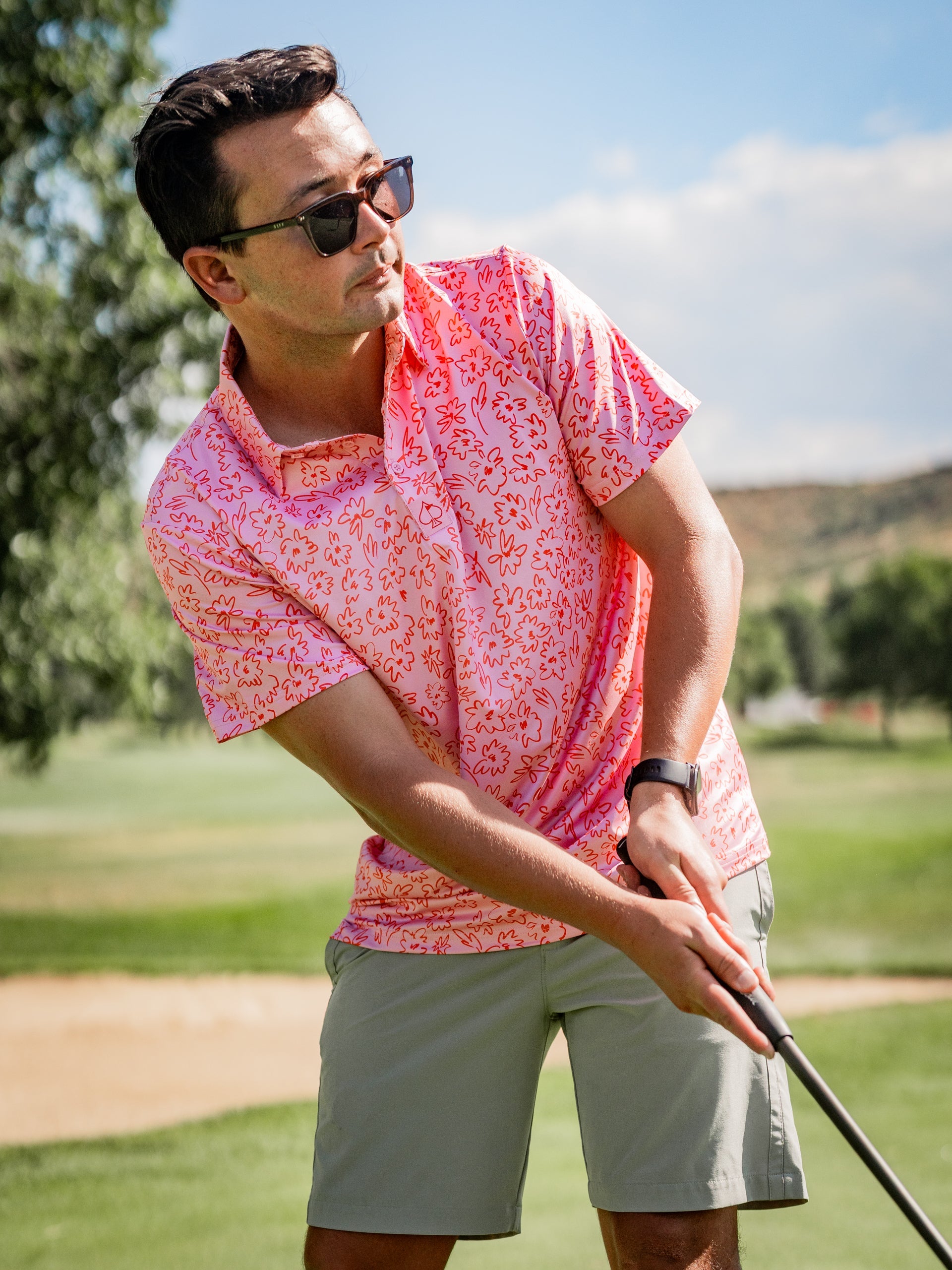 A golfer in a pink floral-patterned polo shirt prepares to swing on the course, showcasing bold golf style.