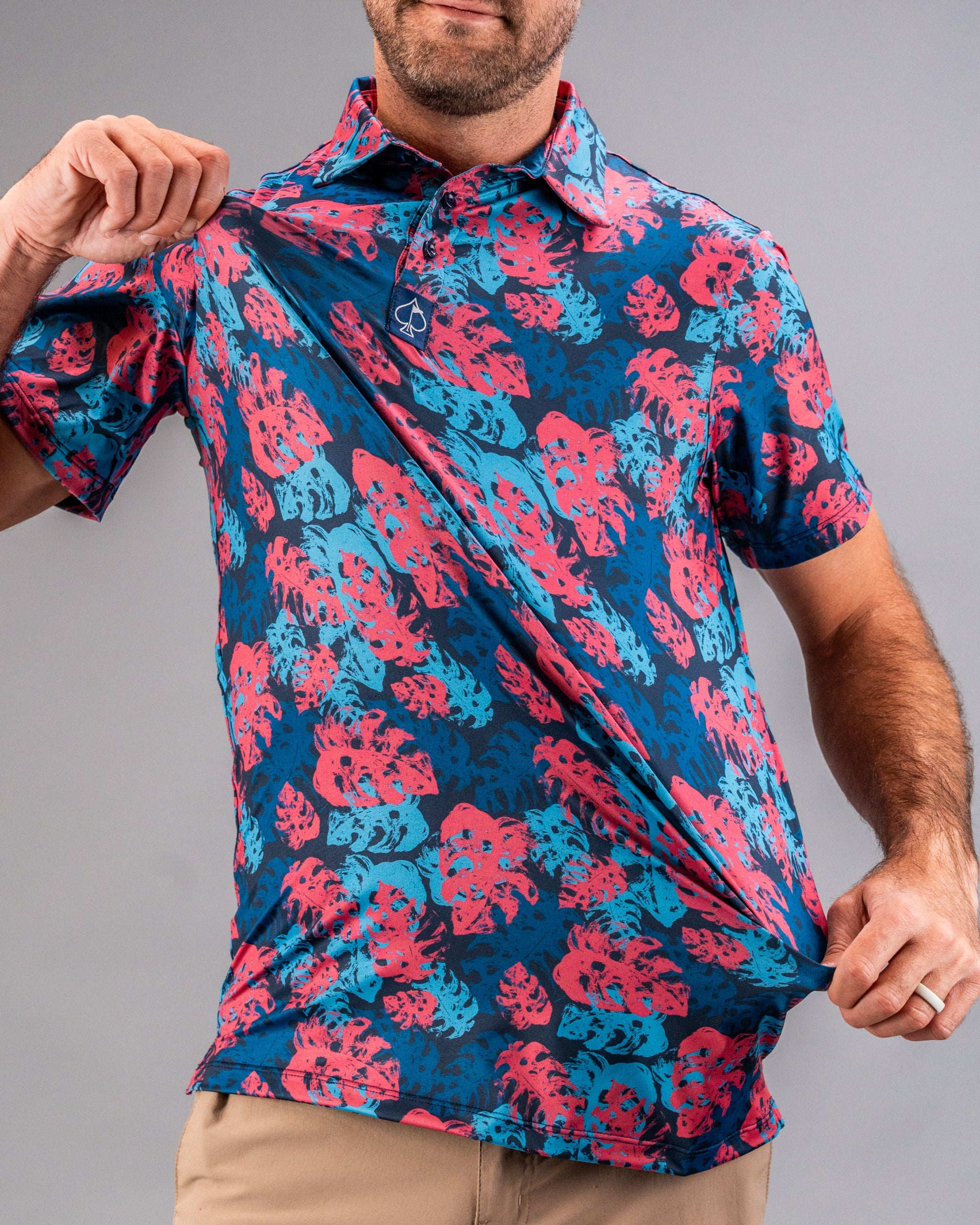 Men's vibrant golf shirt with a bold pink and blue tropical leaf pattern, featuring a small spade logo on the collar.