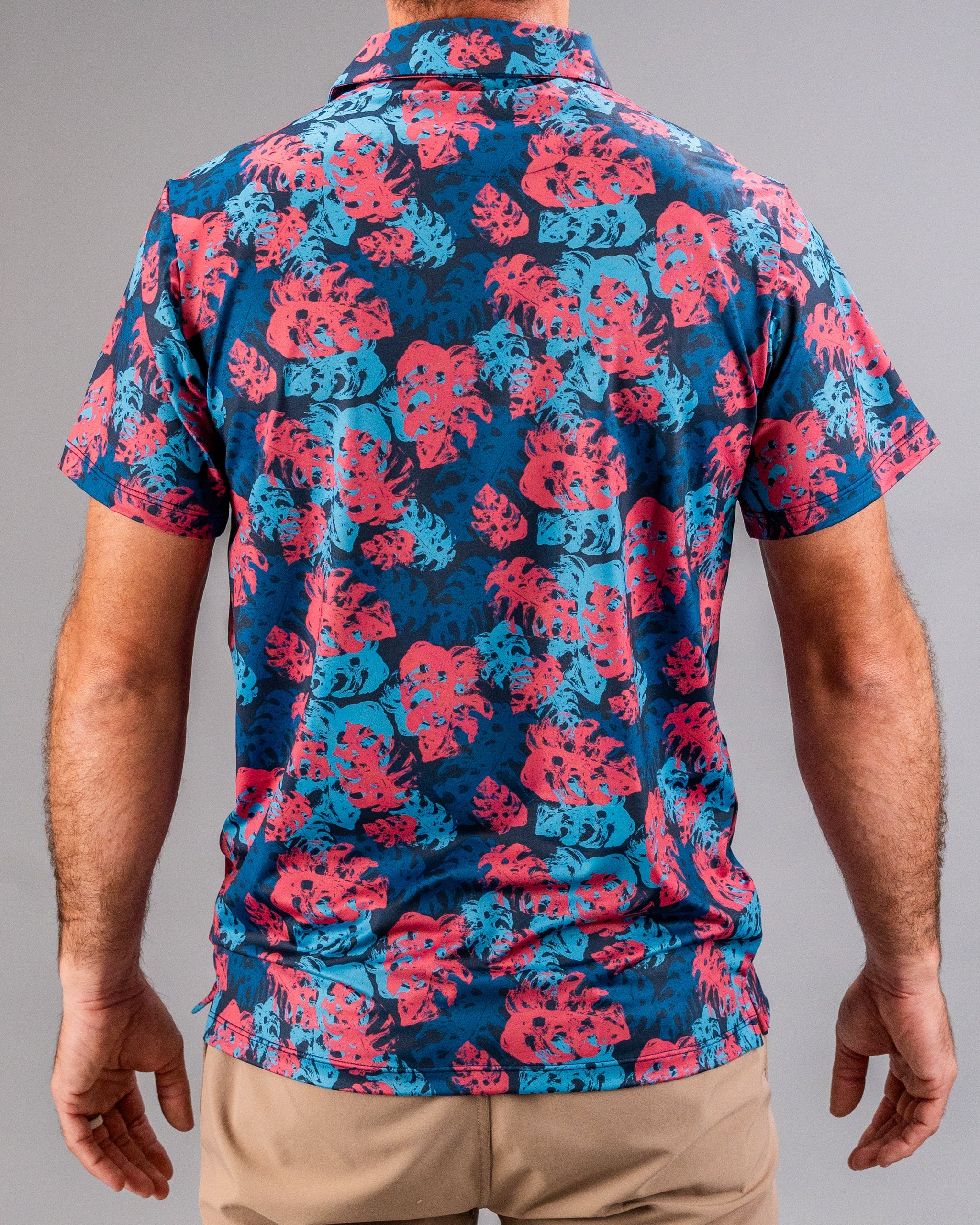 Colorful tropical print polo shirt with pink and blue leaf pattern for bold golf style.