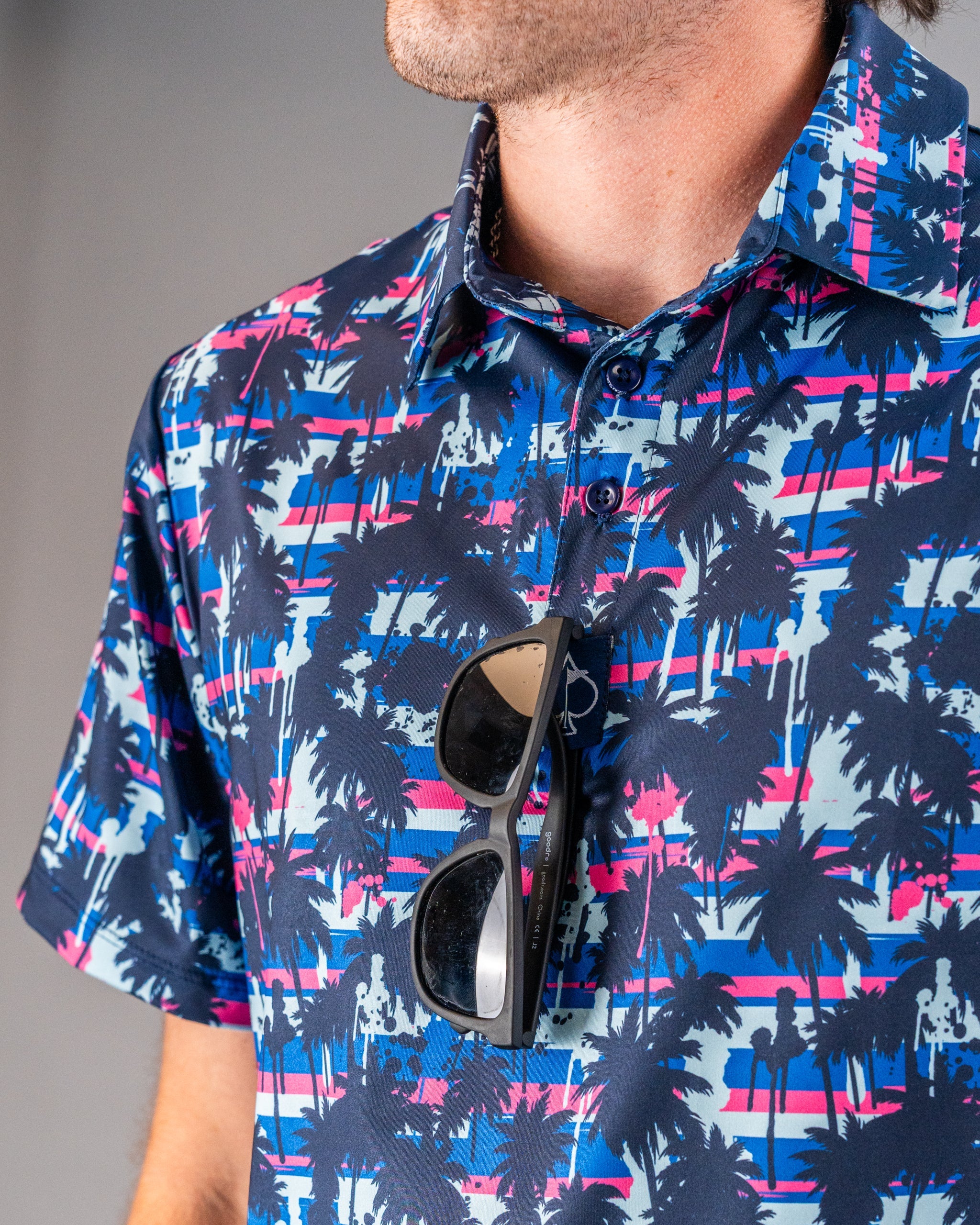 Men's vibrant palm tree golf shirt with pink, blue, and white stripes, featuring bold, tropical-inspired design.