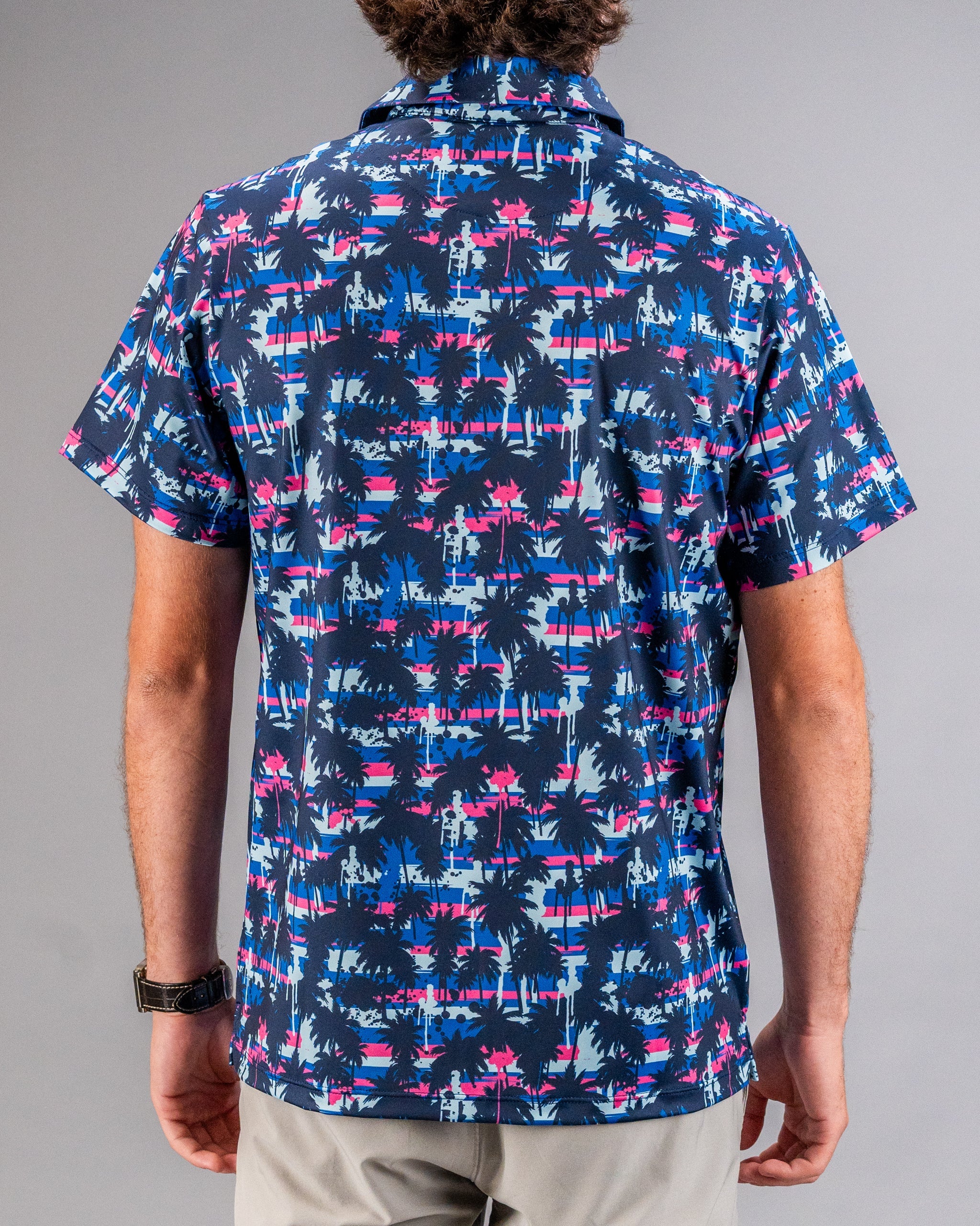 Colorful tropical palm tree print golf shirt featuring pink, blue, and navy hues, perfect for bold golf style.