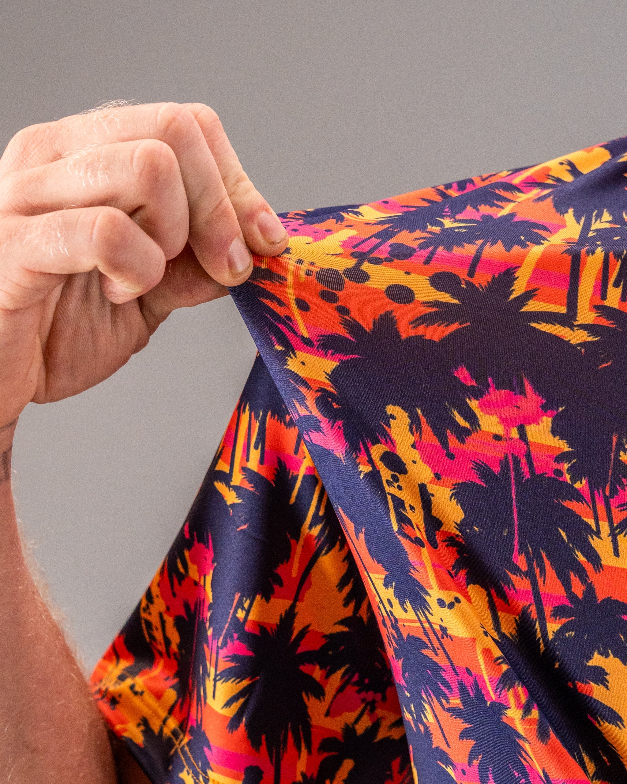 Close-up of a vibrant golf shirt with a tropical sunset and palm tree print in orange, pink, yellow, and navy colors.