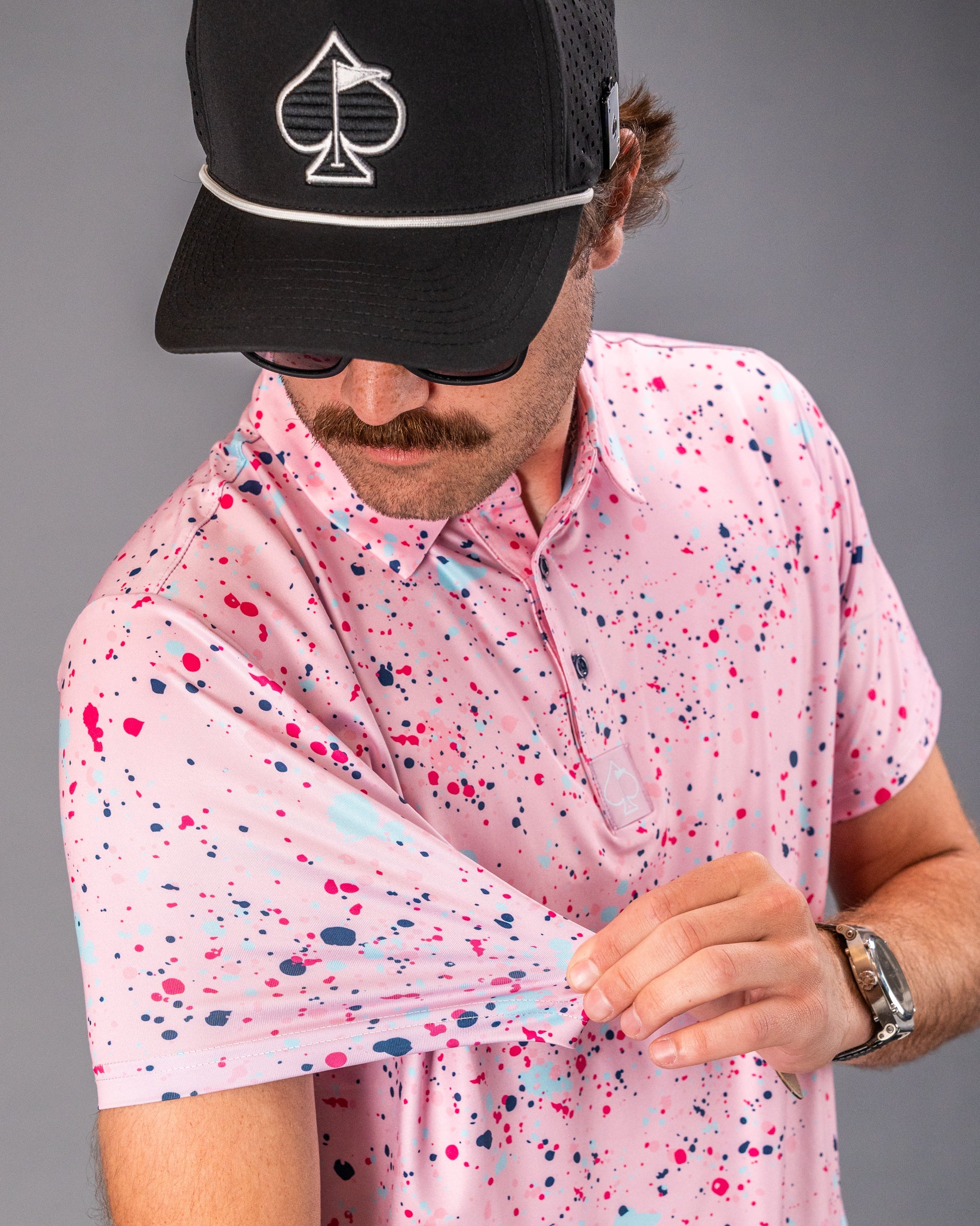 A golfer showcases a pink splatter polo shirt, highlighting its vibrant design and comfortable fit.