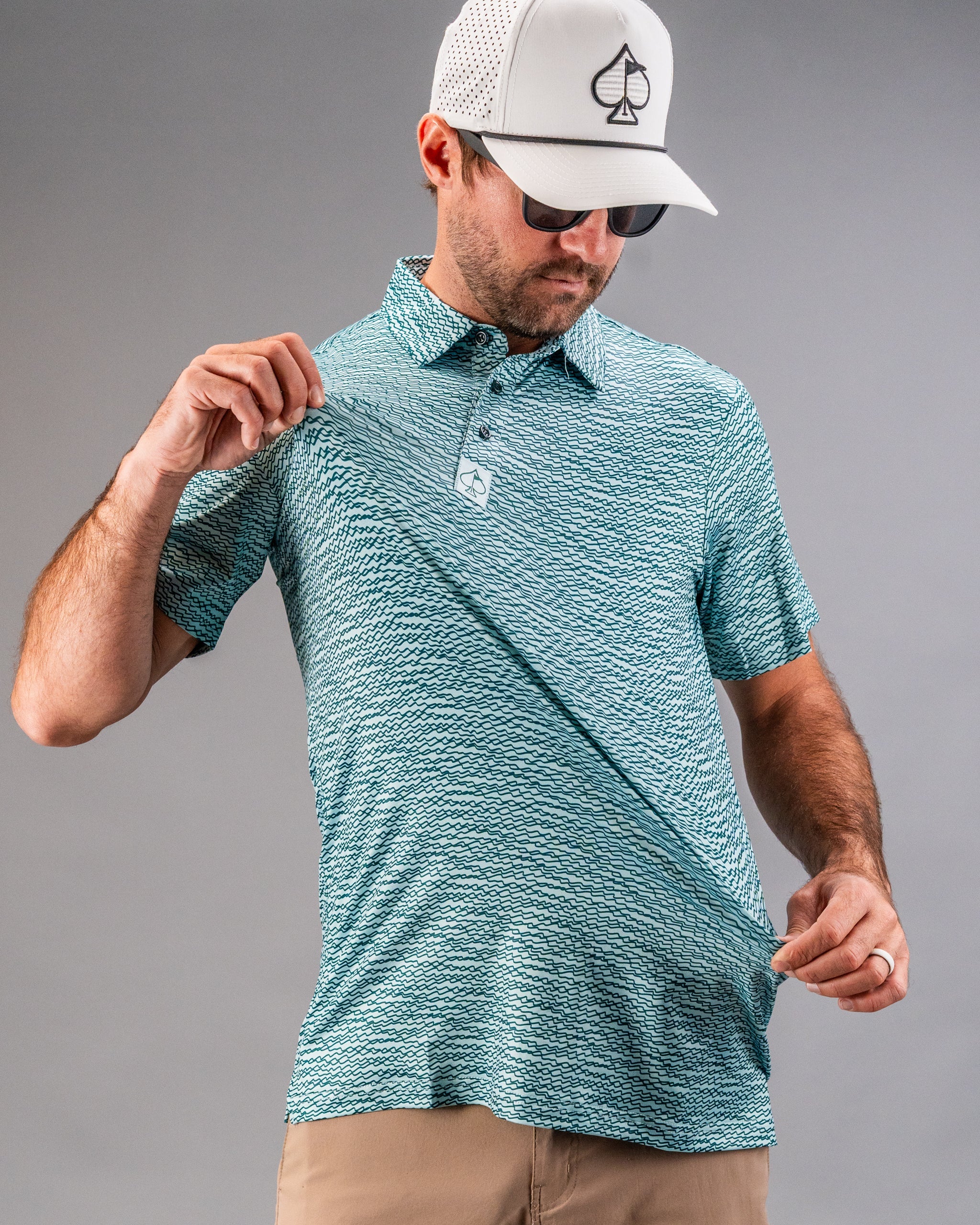 Teal golf polo shirt with a squiggle pattern, worn by a man adjusting the fabric, showcasing its stylish design.