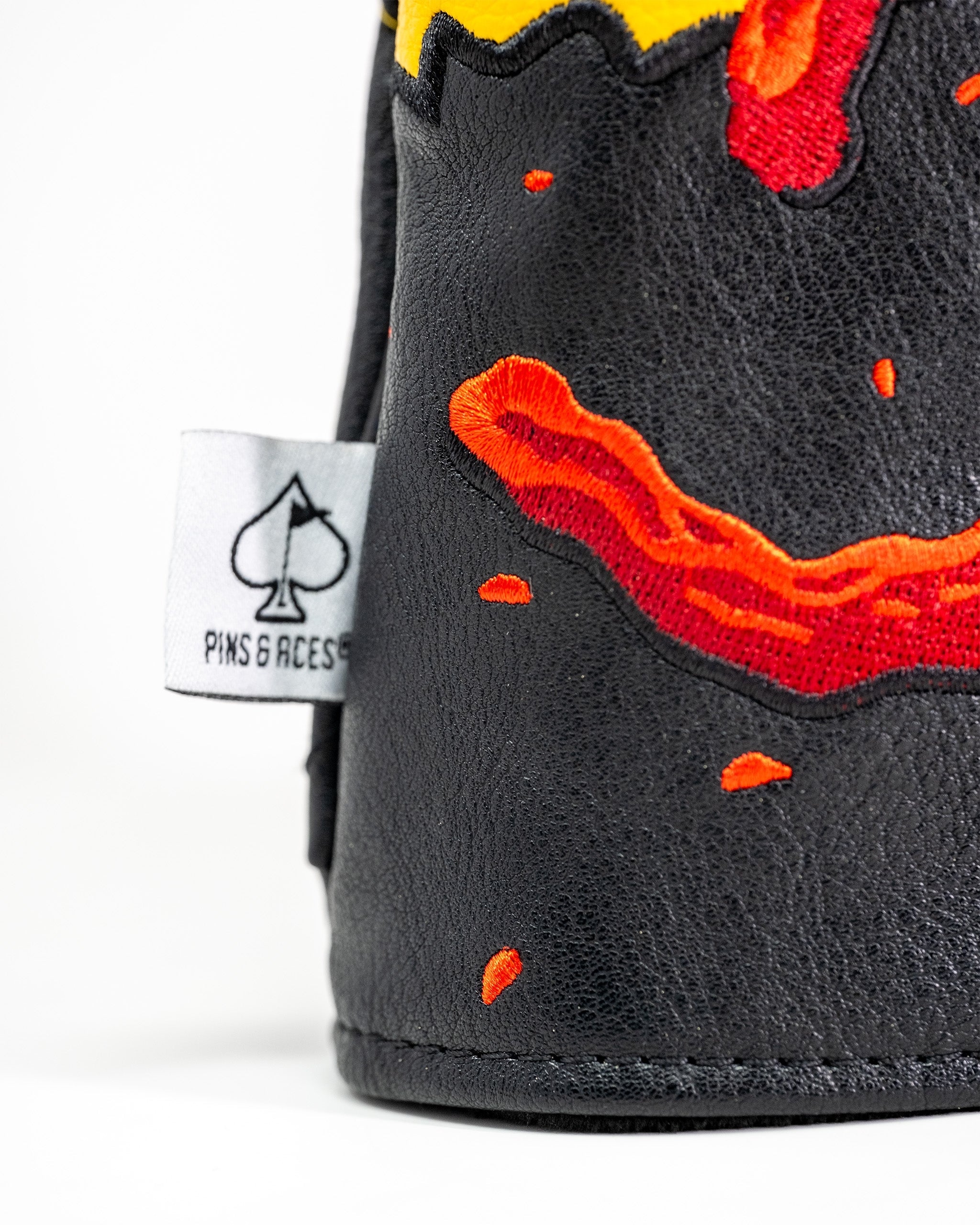 Close-up of a black golf driver cover with embroidered flaming hot chili pepper design and a Pins and Aces tag.