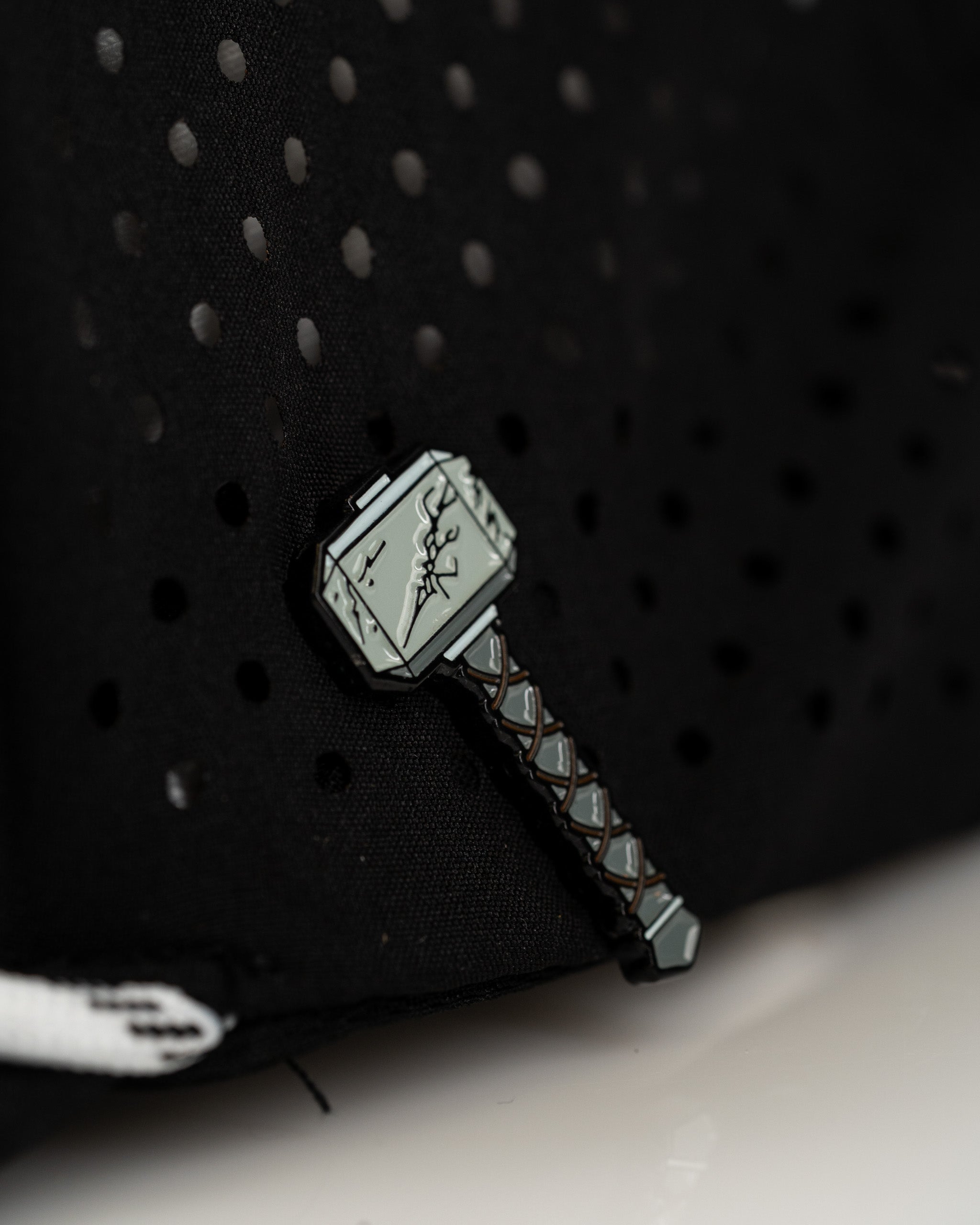 Black perforated rope hat featuring a detailed Thor's Hammer pin, perfect for bold golf enthusiasts.