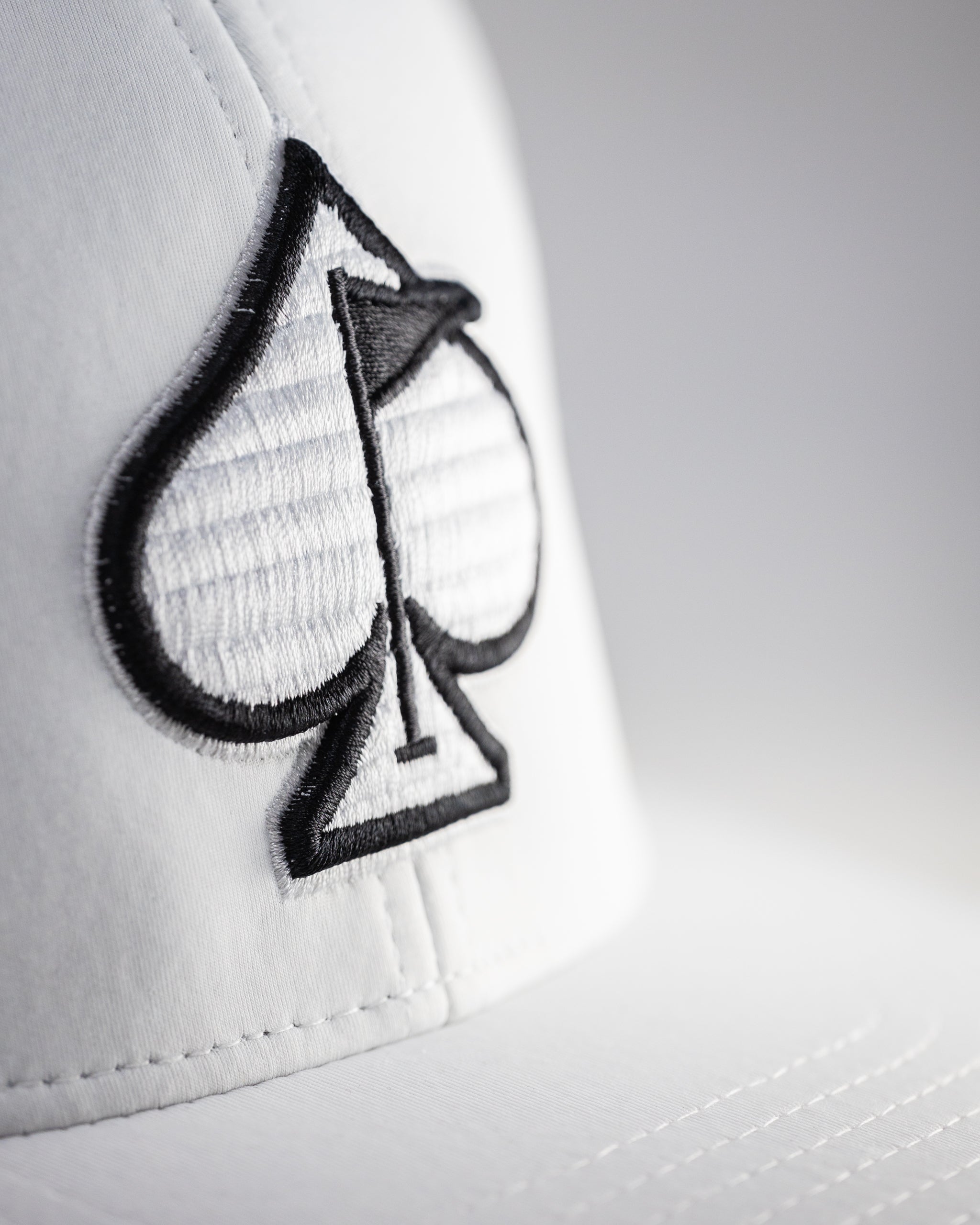 Performance Spade Hat in white, featuring a sleek design and an adjustable strap. Ideal for outdoor activities.