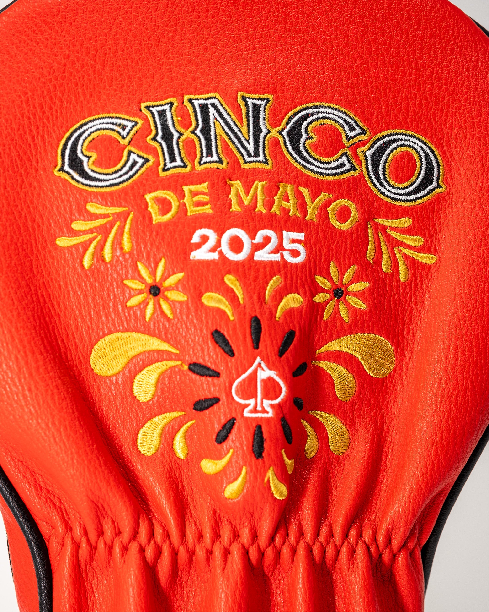 Red lucha libre mask driver cover with embroidered "Cinco de Mayo 2025" design, yellow and black decorative details, and a spade symbol.