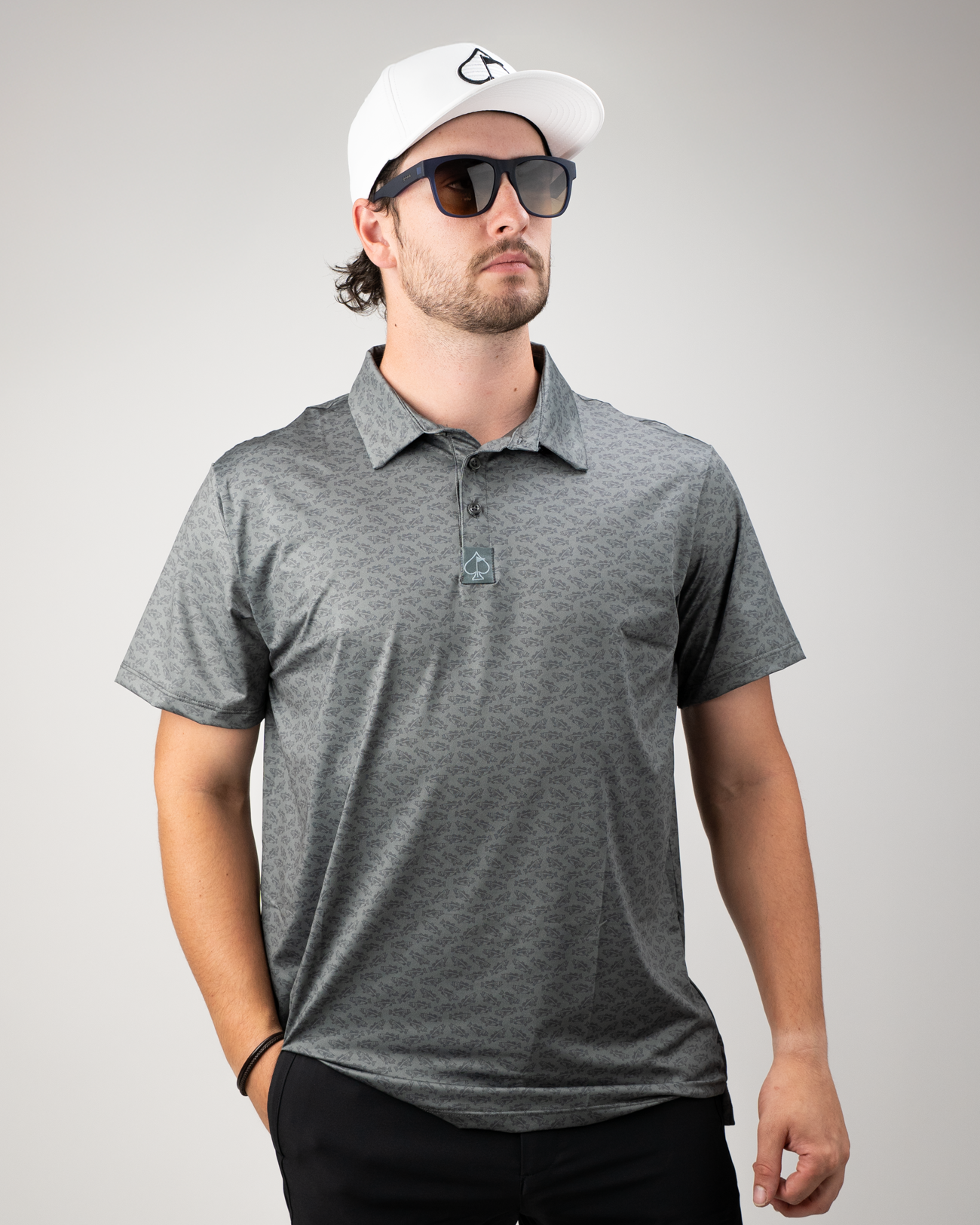 Man wearing a gray patterned golf polo shirt with a collar, sunglasses, and a white cap, posing confidently.