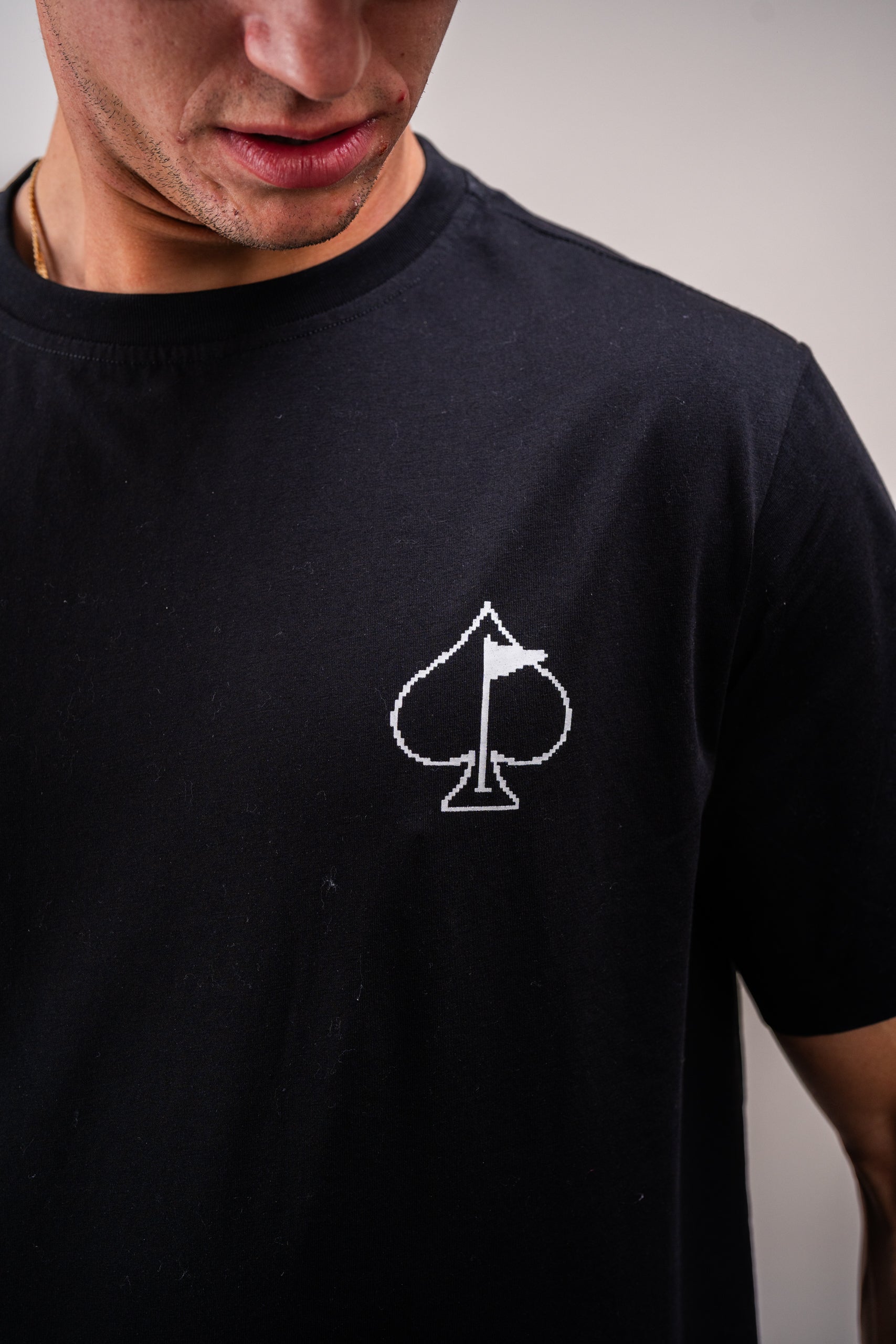 Close-up of a man wearing a black t-shirt featuring a white 8-bit style spade symbol on the chest.