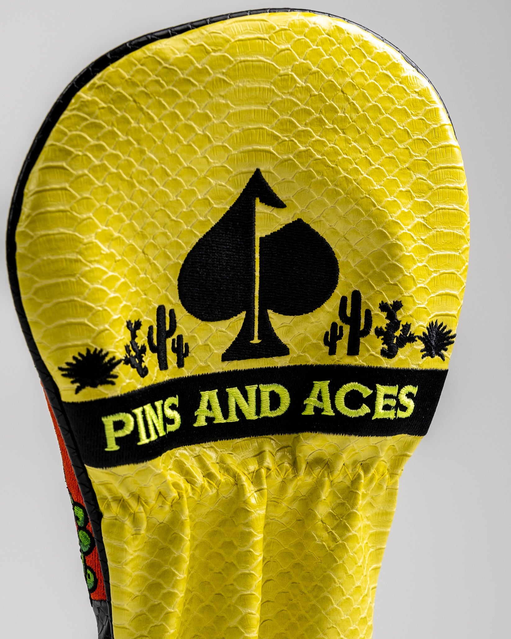 Bright yellow golf headcover with black embroidered cactus, spade, and "PINS AND ACES" text, featuring bold, unique golf a...