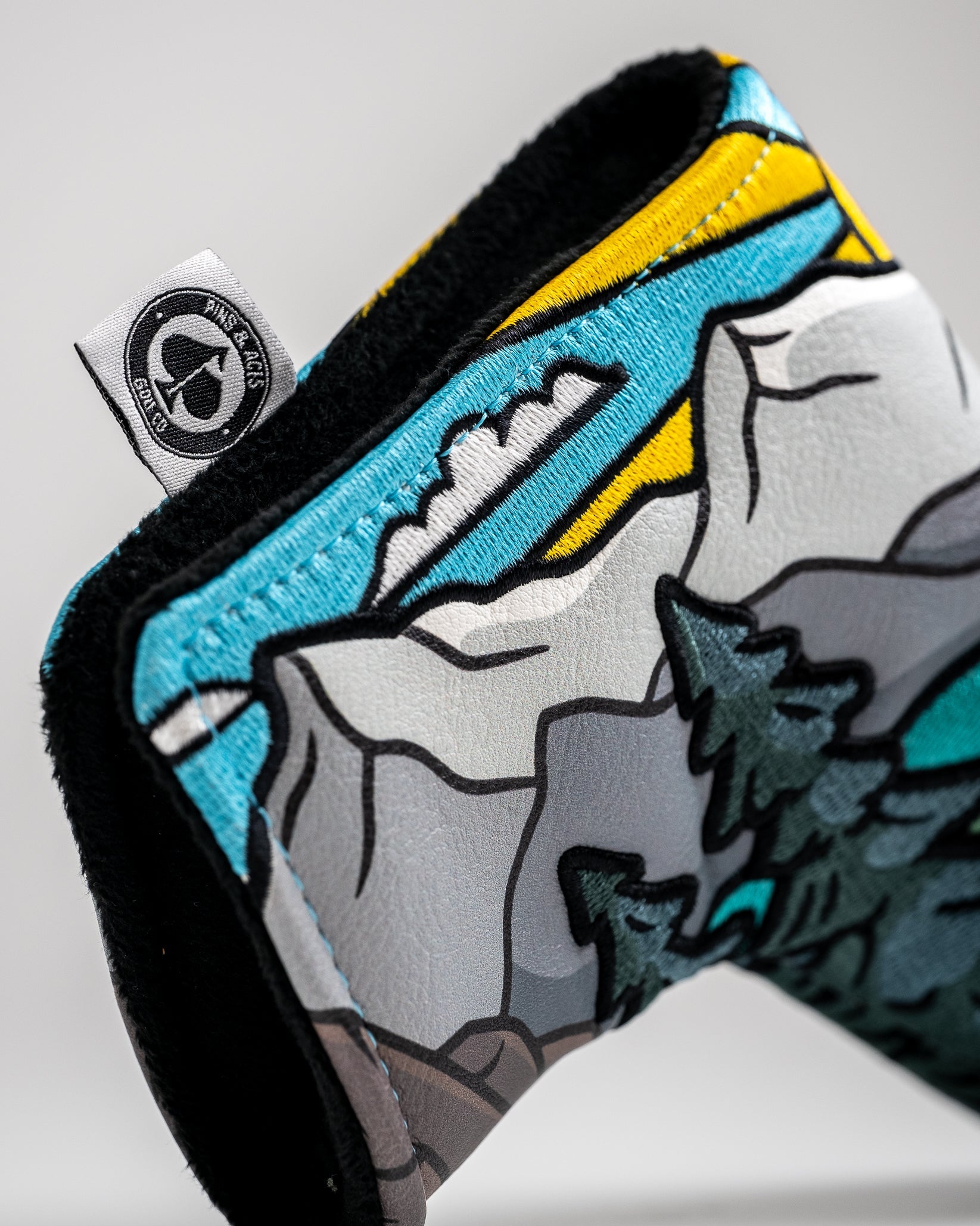 Colorful, bold golf headcover with mountain and forest design, featuring bright blue, yellow, white, and black accents.