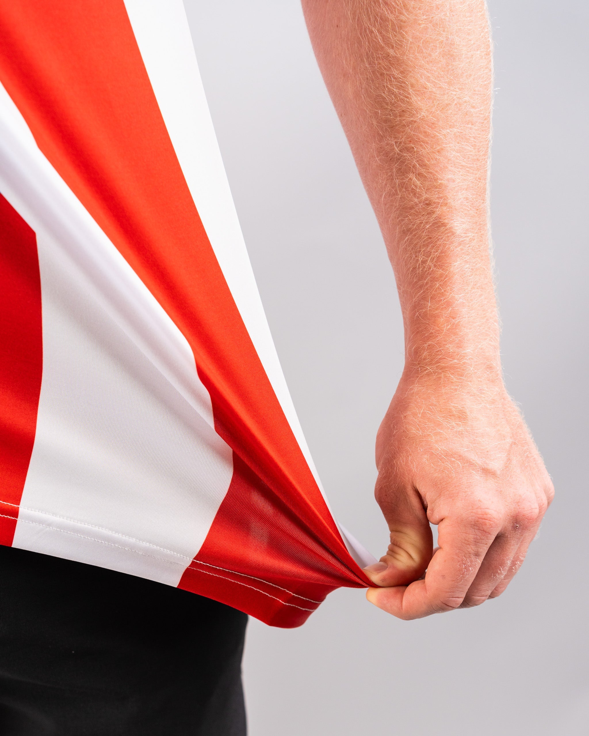 Close-up of a person holding the corner of a red and white American flag, with visible arm and hand against a plain background.