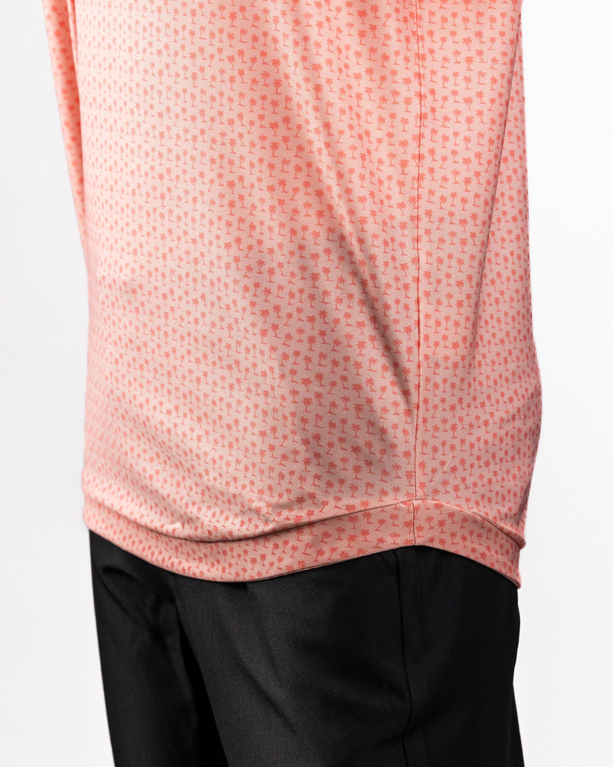 Close-up of a coral pink Player Preferred™ Polo shirt with a small palm tree pattern, paired with black pants.