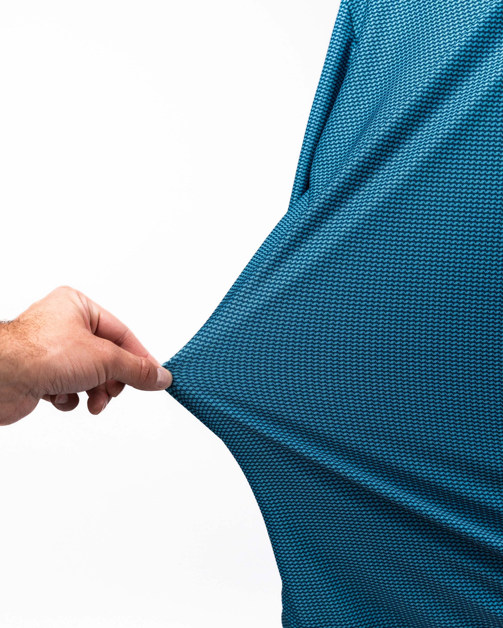 Close-up of a hand pulling the fabric of a blue Player Preferred™ Polo - Ocean Wave shirt, showing its textured, patterned material.