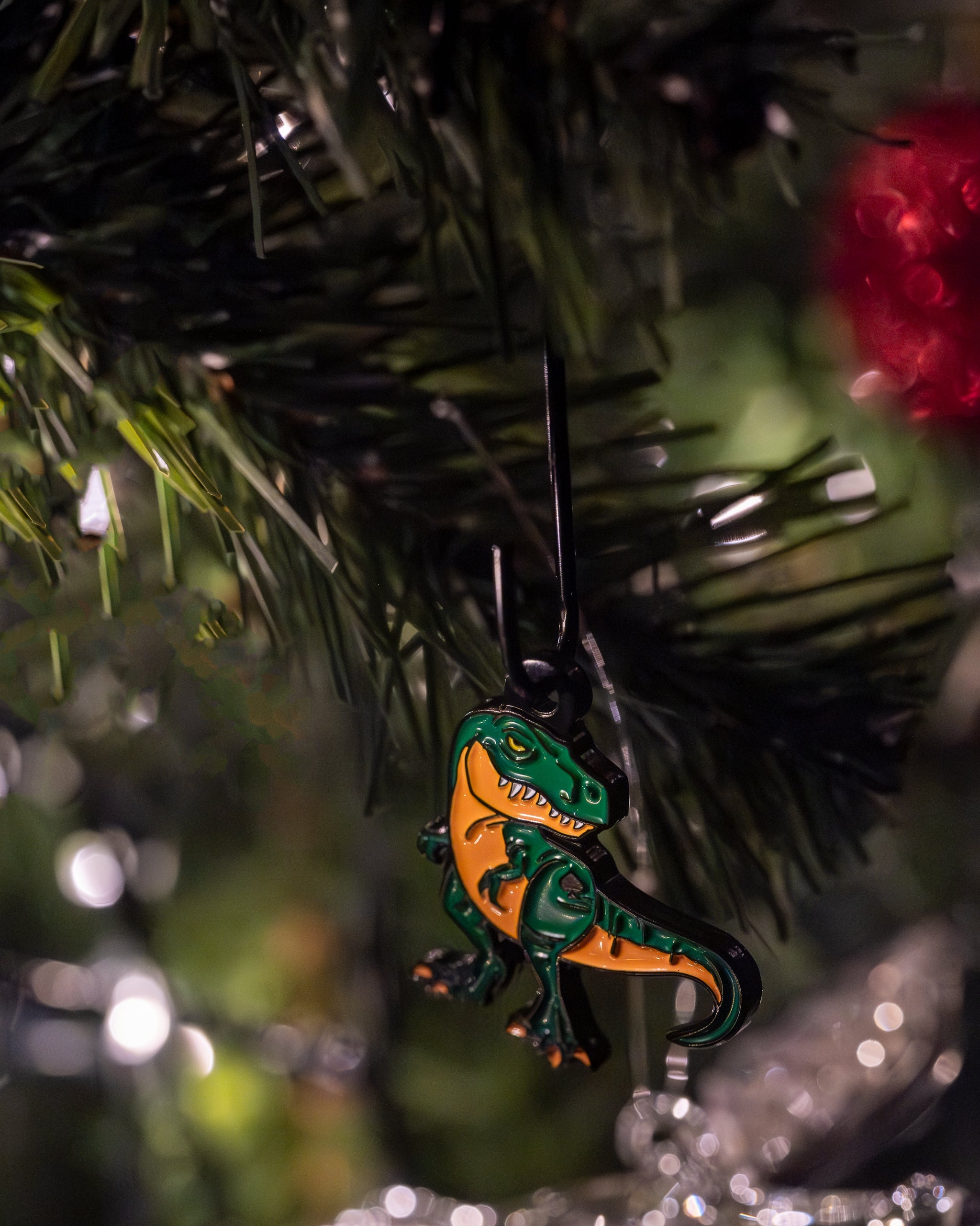 T-Rex dinosaur ornament with vibrant green and yellow colors, featuring detailed scales and a playful expression, hanging from a red ribbon.