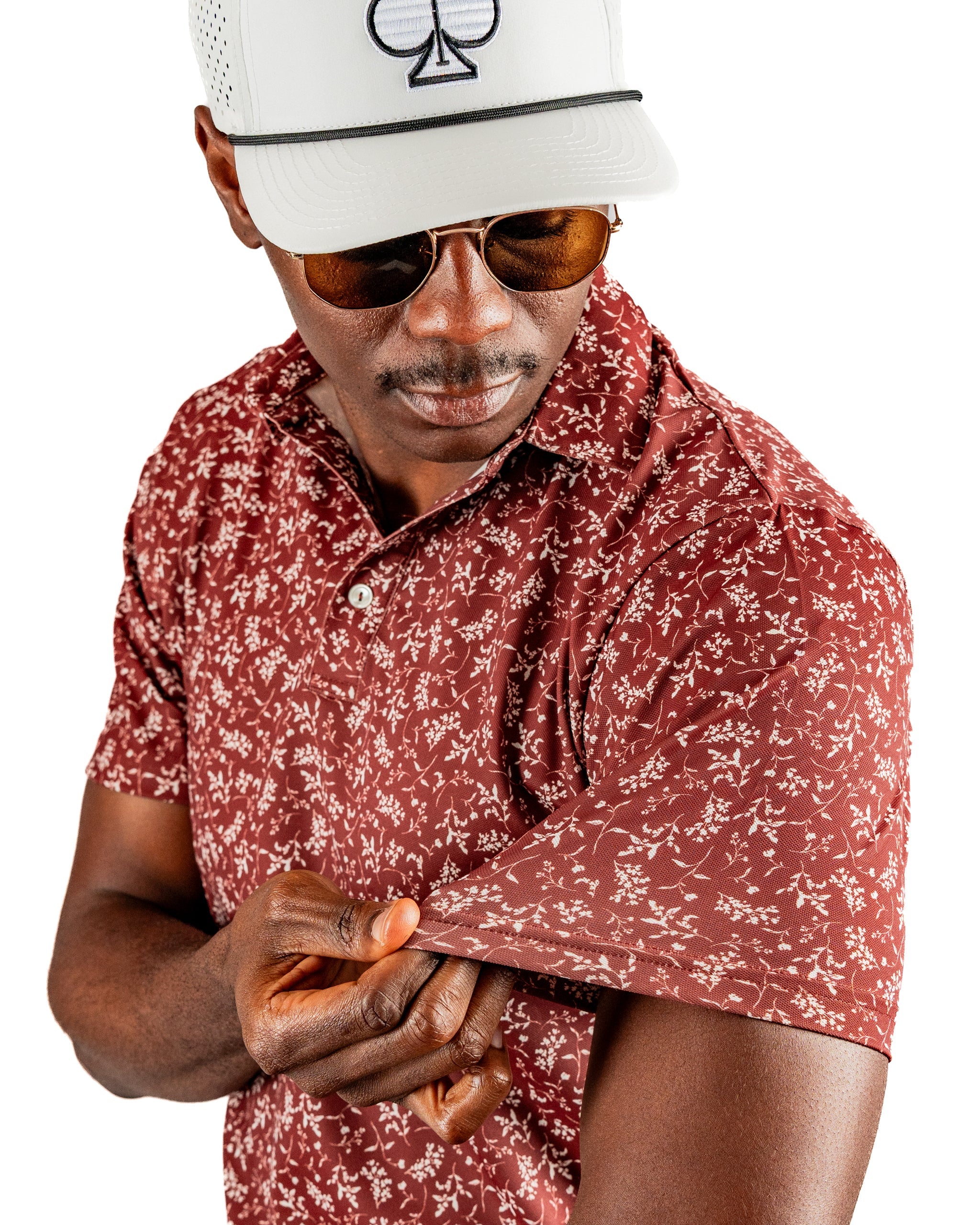 Stylish man in a maroon floral polo shirt, adjusting the sleeve, showcasing a bold and unique golf fashion choice.