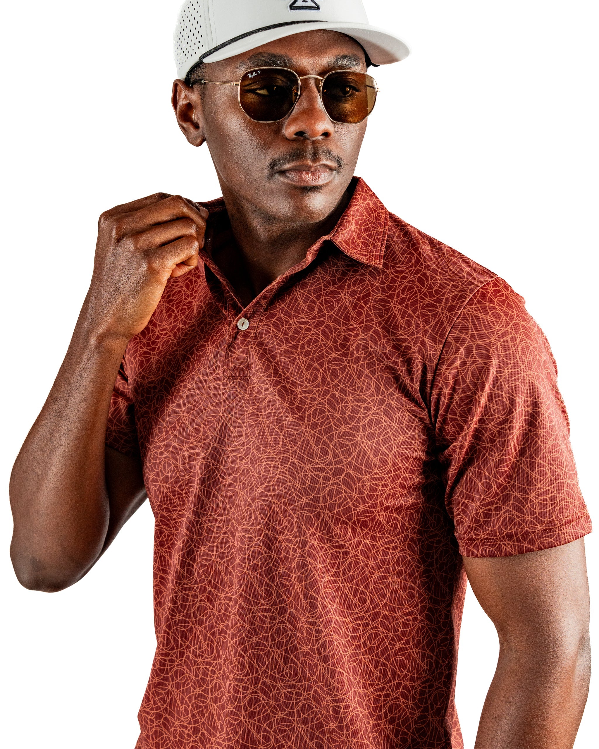 Stylish golfer wearing a patterned red polo shirt, sunglasses, and a white cap, showcasing bold golf apparel.