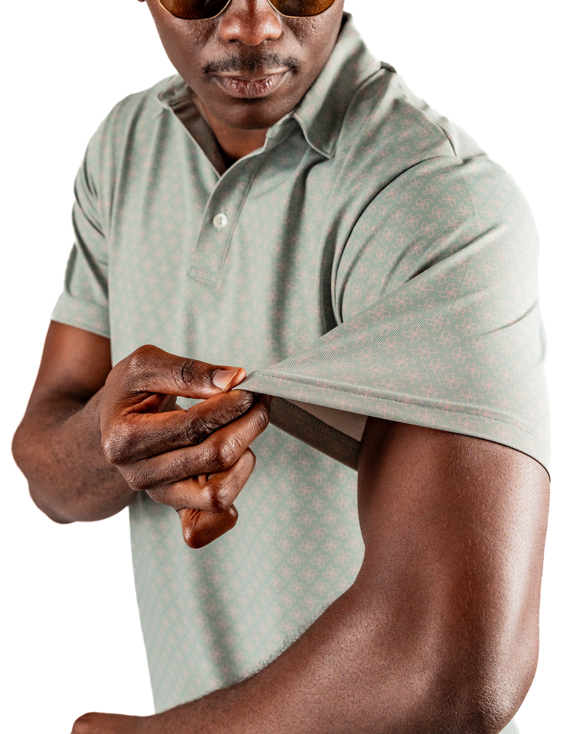A man in sunglasses adjusts the sleeve of a light green polo shirt featuring a subtle pattern, showcasing its fit and style.