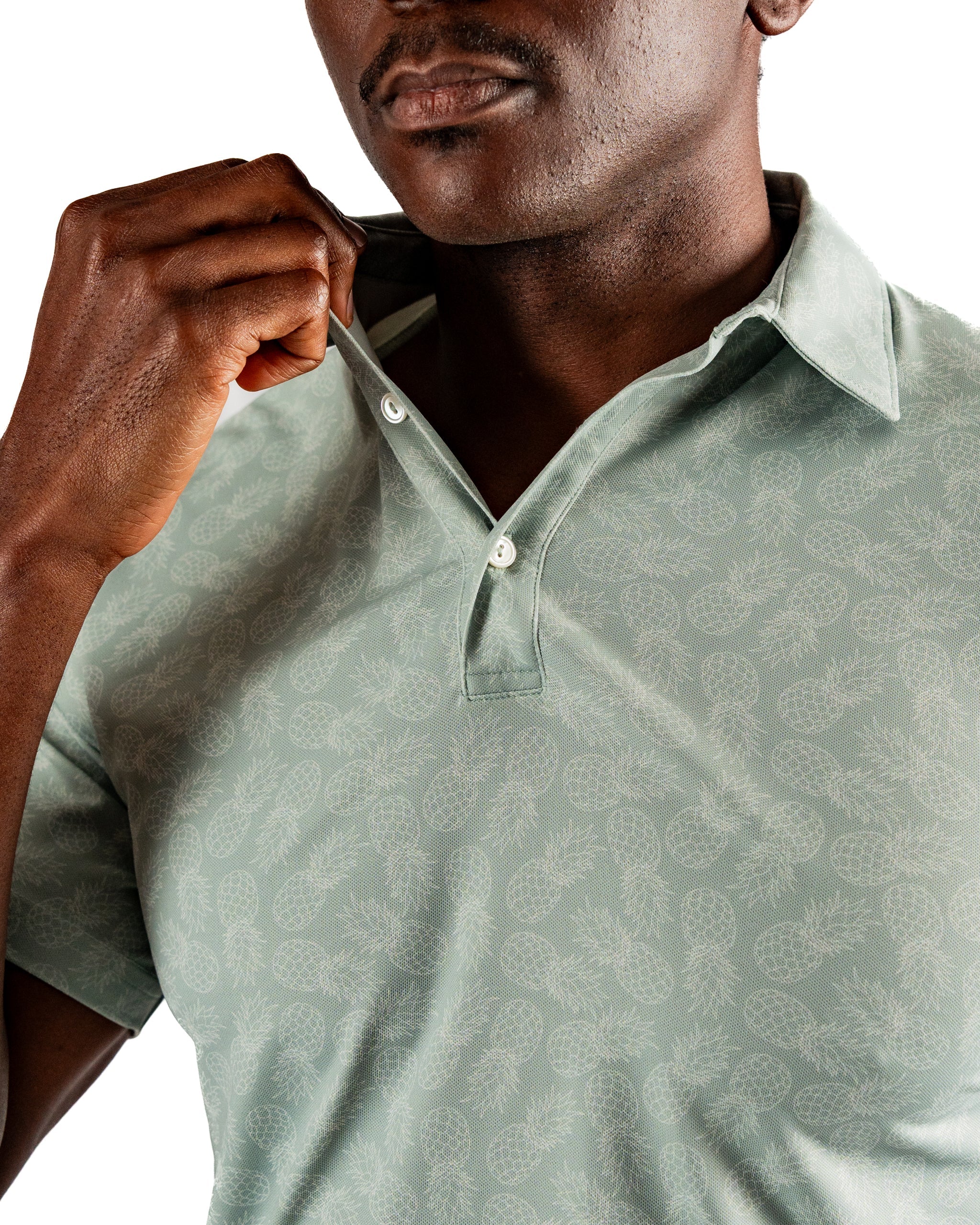 A man adjusts the collar of a light green polo shirt featuring a subtle pineapple pattern, showcasing a stylish golf look.