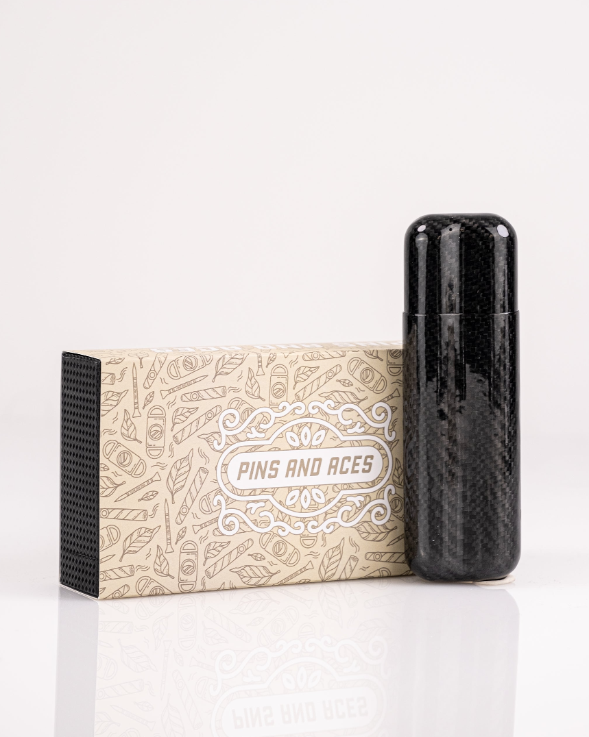 Sleek carbon fiber cigar case with two slots, displayed next to a decorative box featuring the Pins and Aces logo.