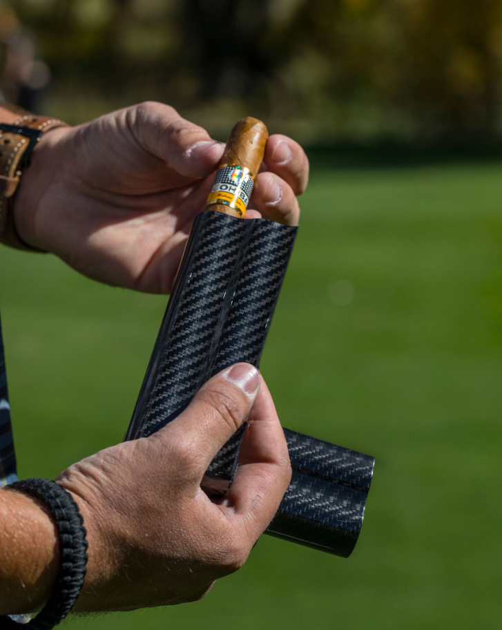 Carbon fiber cigar case with two slots, holding a cigar, ideal for golfers who enjoy luxury accessories on the course.