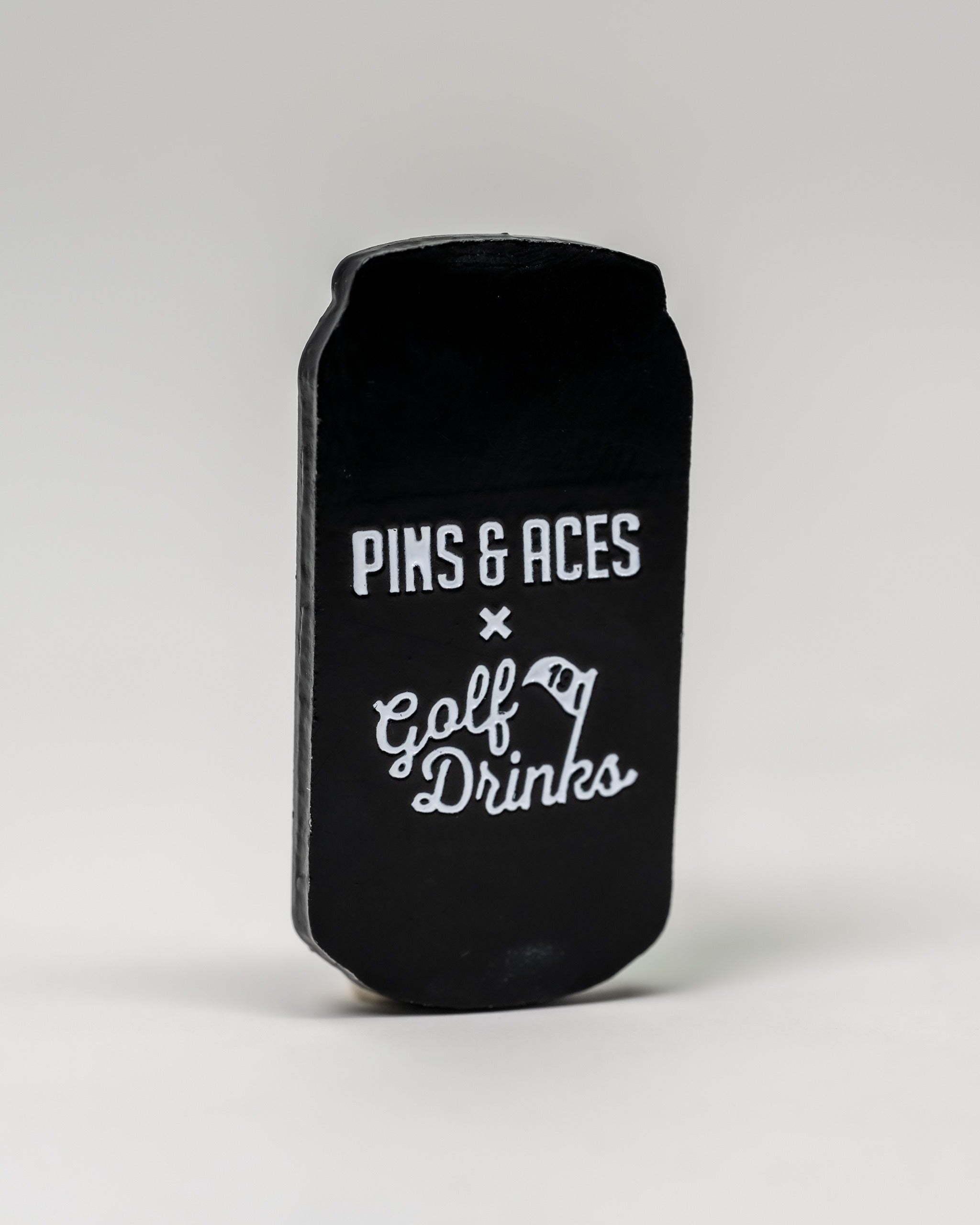Black transfusion can ball marker featuring "Pins & Aces" and "Golf Drinks" branding for stylish golf play.