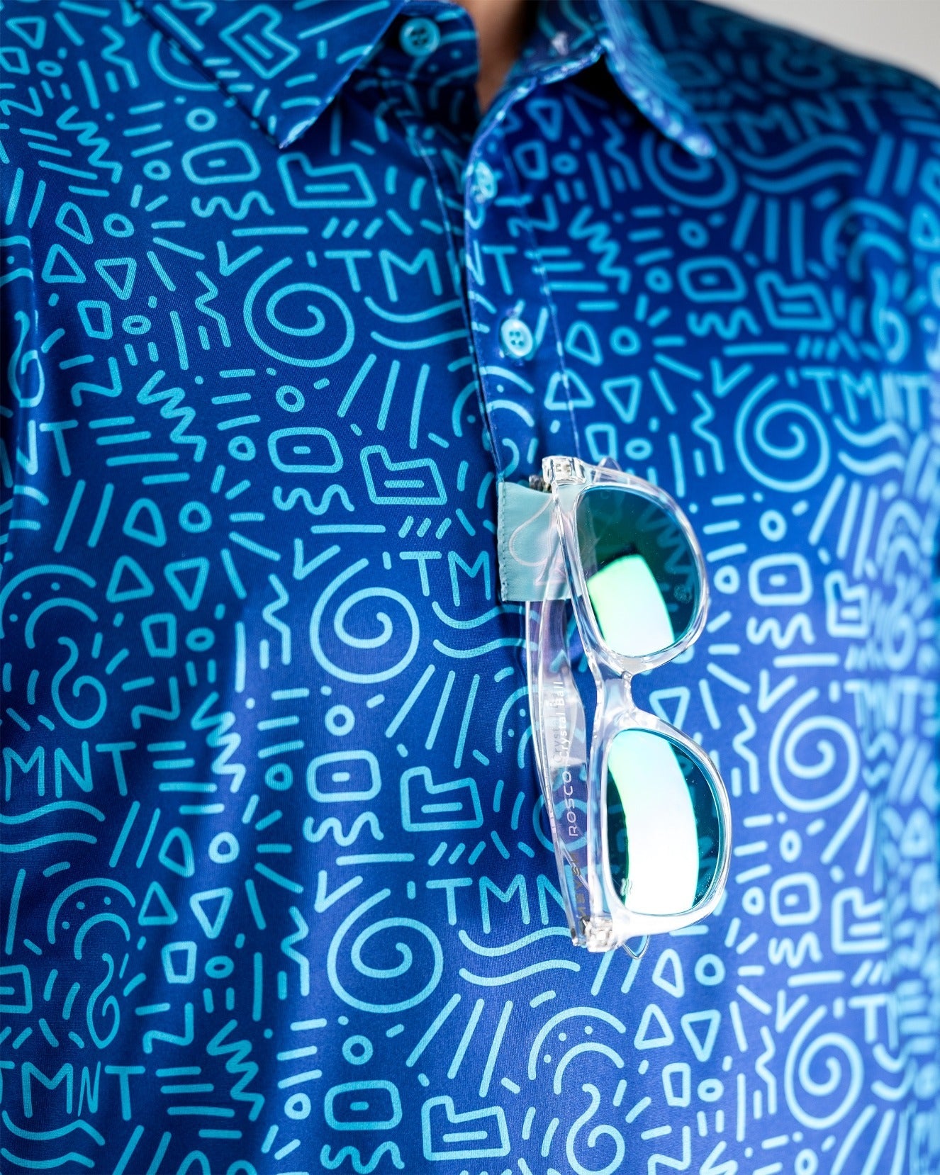 Bold blue golf shirt featuring a playful doodle pattern with TMNT graphics, paired with stylish sunglasses.