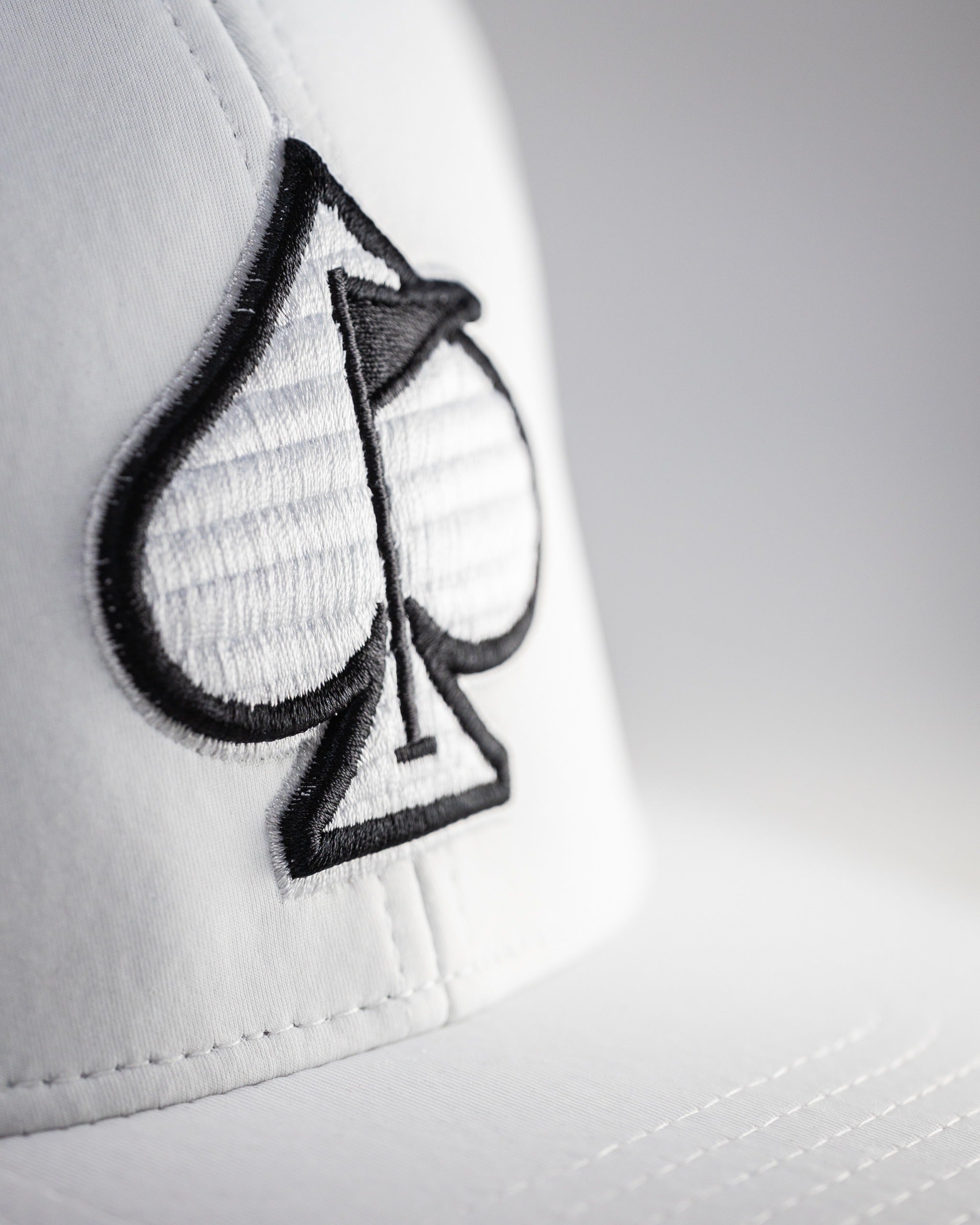 White Performance Spade Hat featuring a bold black spade logo, designed for stylish golfers seeking standout accessories.