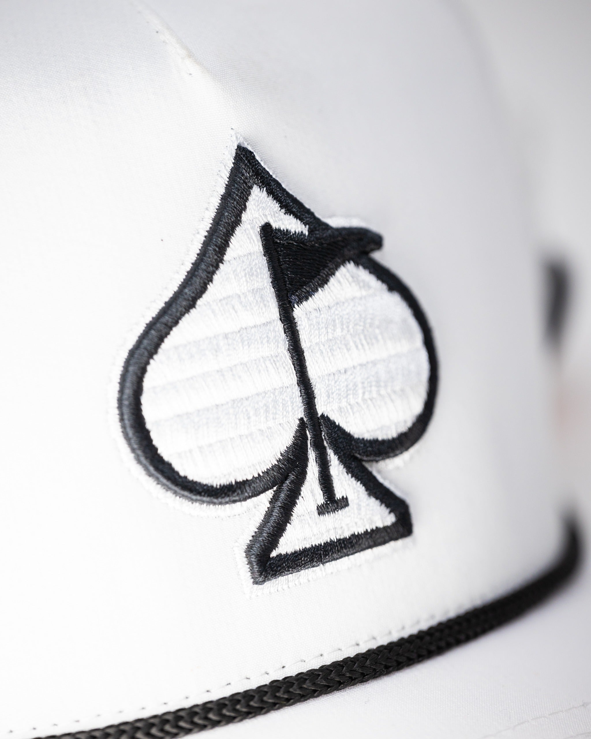 White perforated rope hat featuring a black spade logo with a flag, designed for stylish golfers.