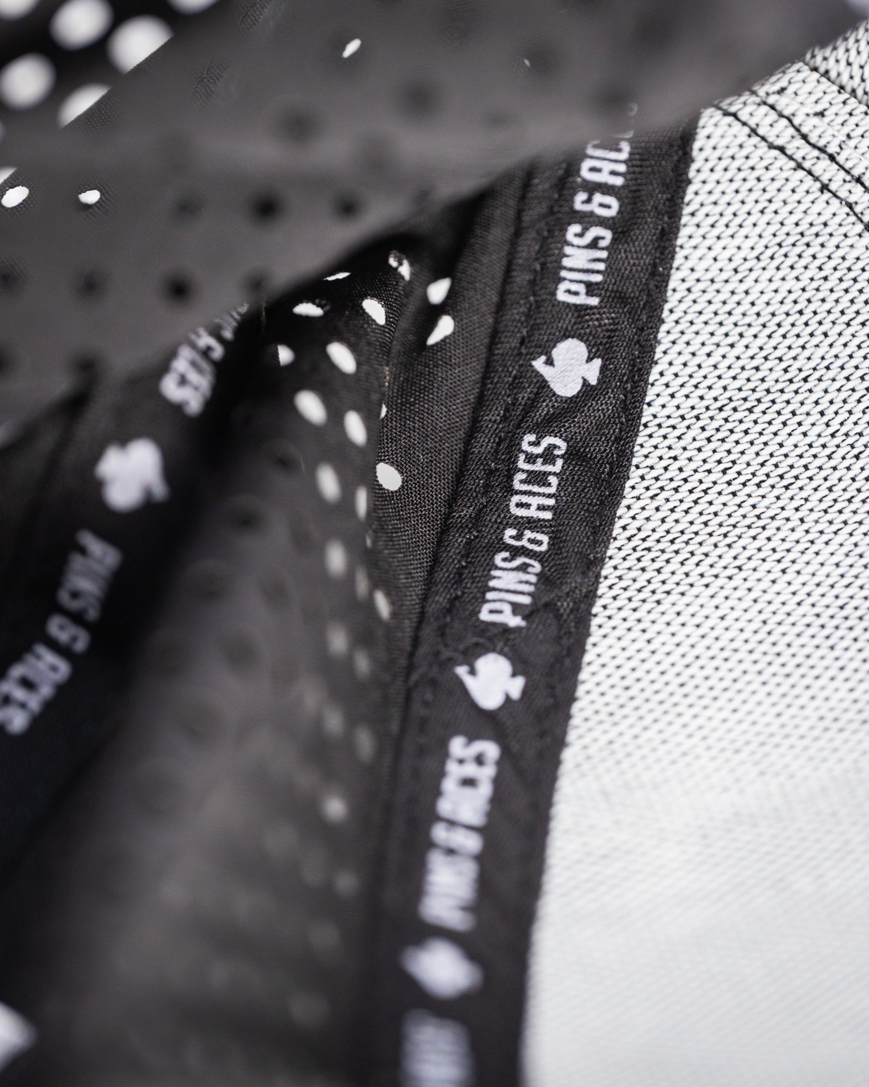 Close-up of the black perforated rope hat showcasing breathable fabric and the Pins and Aces logo on the inner band.