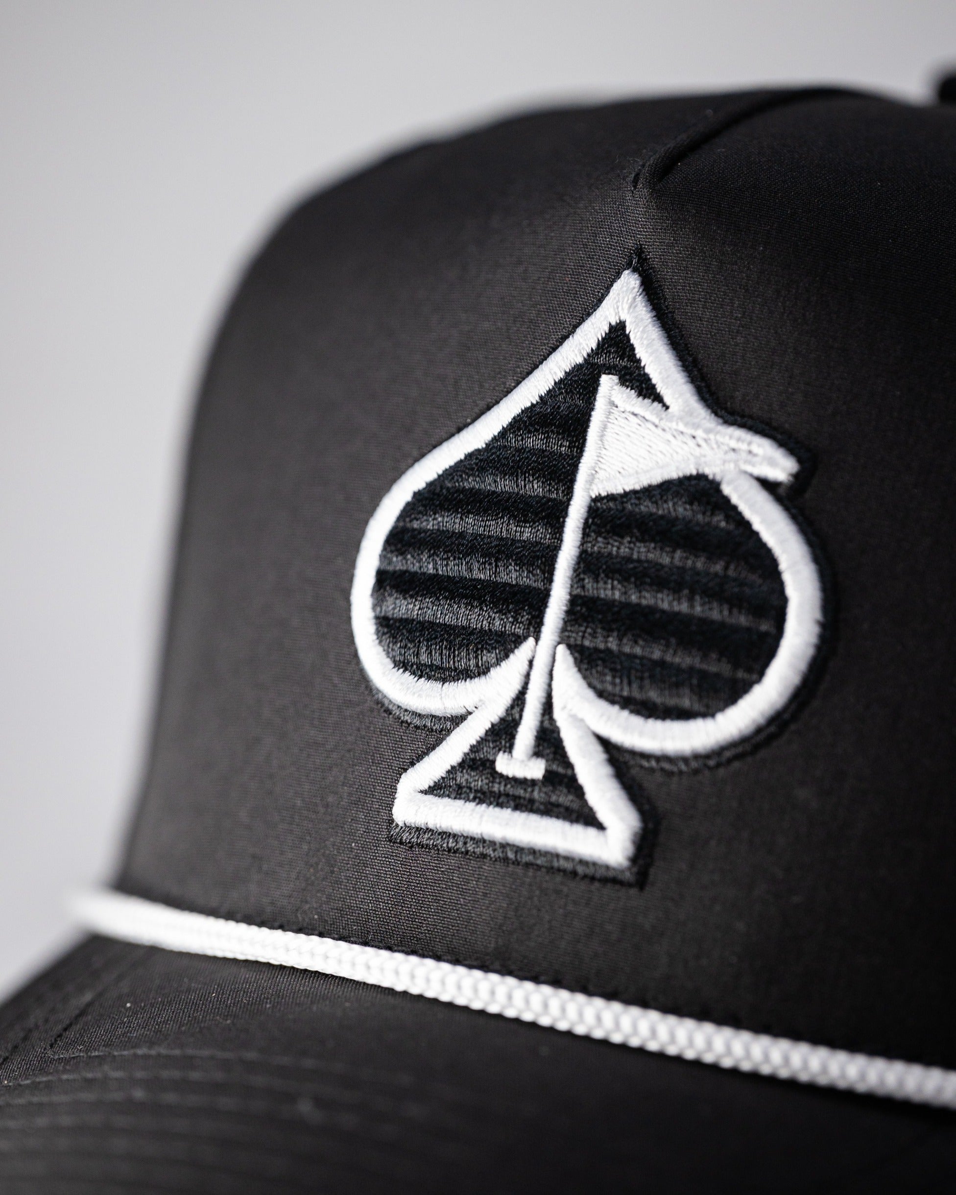 Black perforated rope hat featuring a stylish spade logo and a white accent band, perfect for bold golfers.