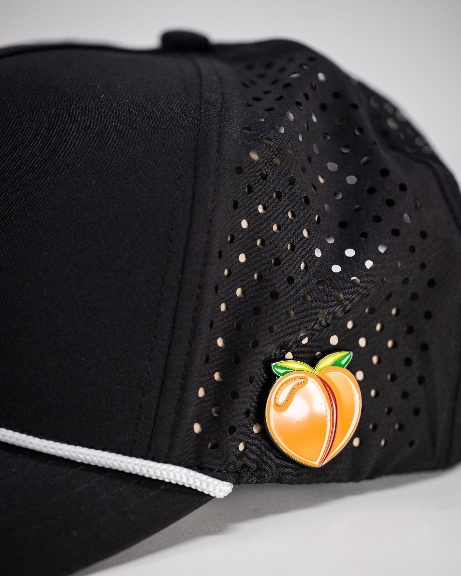 Black perforated rope hat featuring a colorful peach pin on the side, designed for stylish golfers.