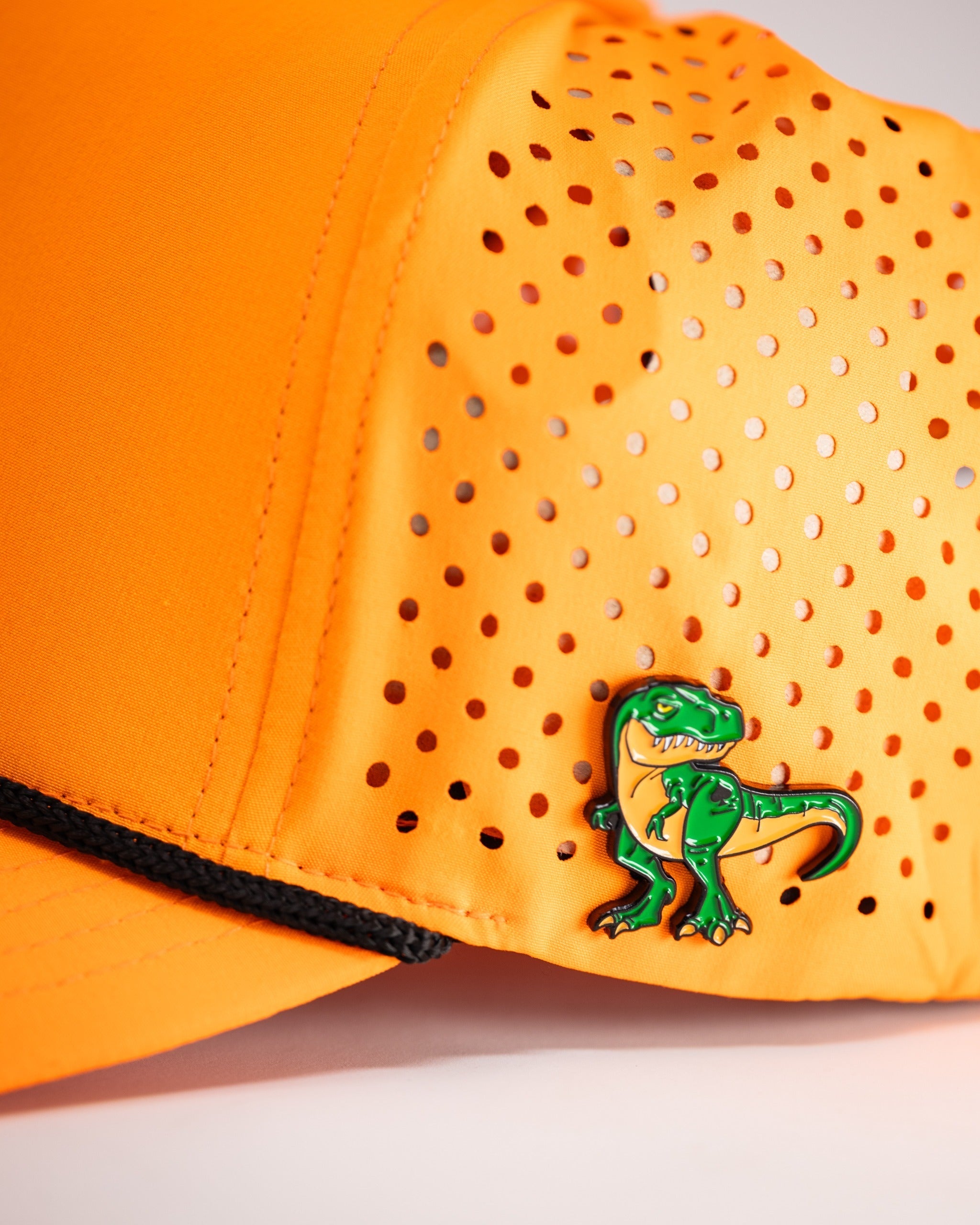 Highlighter orange perforated rope hat featuring a playful green dinosaur pin for a bold golf style.
