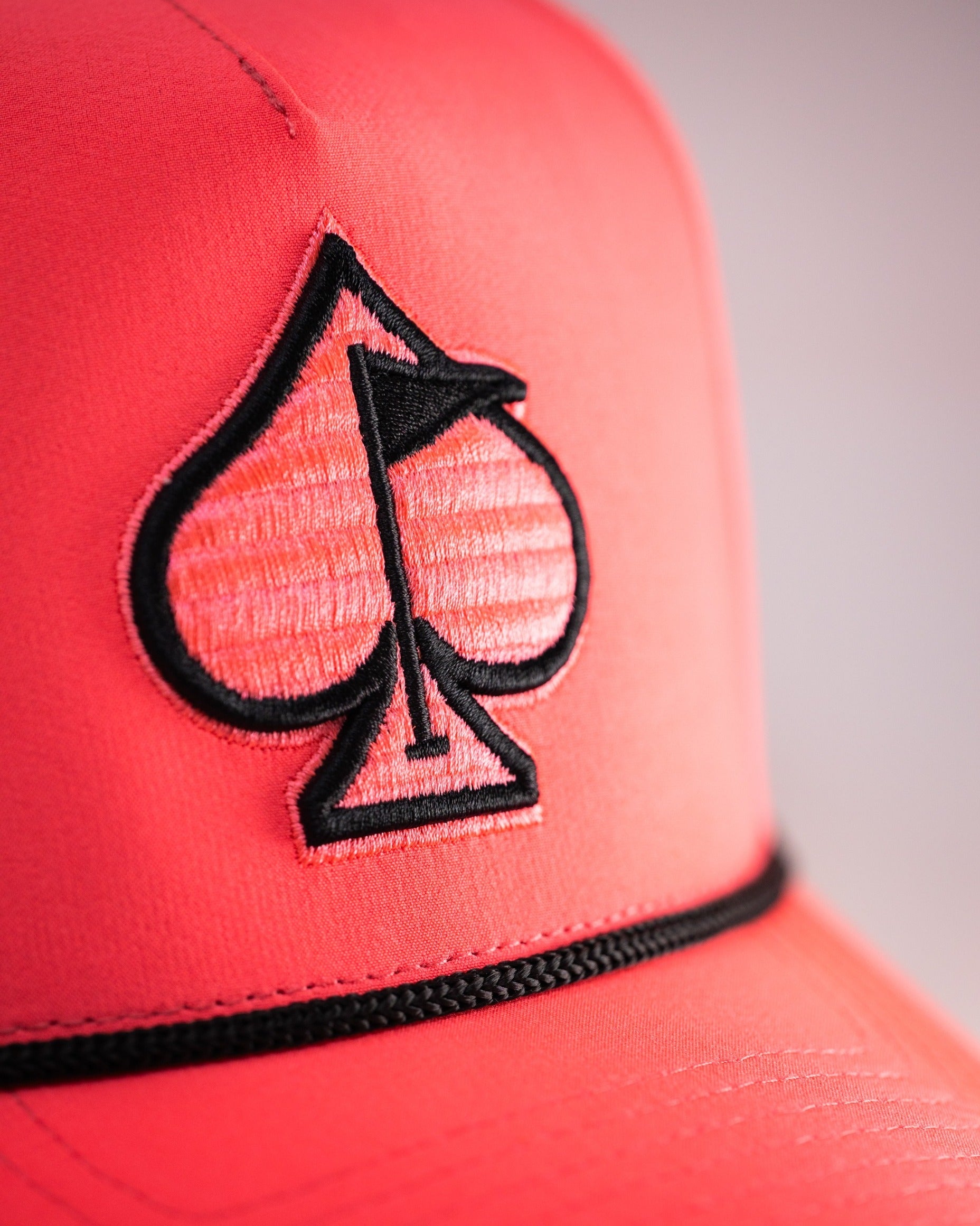 Highlighter pink perforated rope hat featuring a black embroidered spade logo, perfect for stylish golfers.