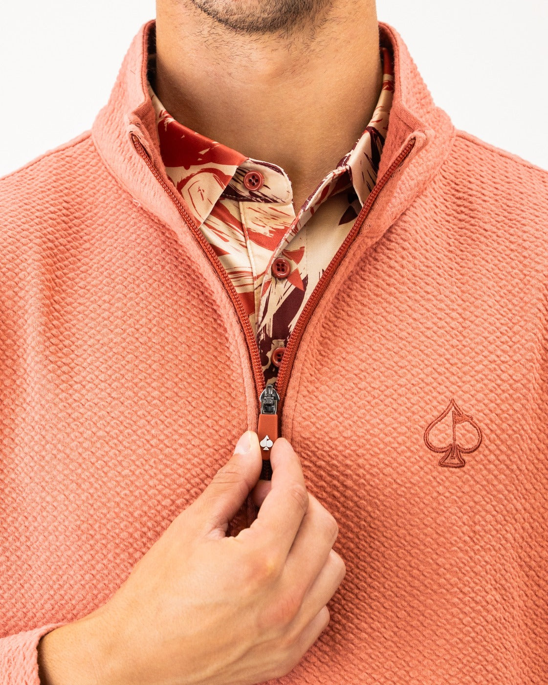 Terracotta waffle knit pullover with a half-zip and logo, layered over a patterned shirt, showcasing a stylish golf look.