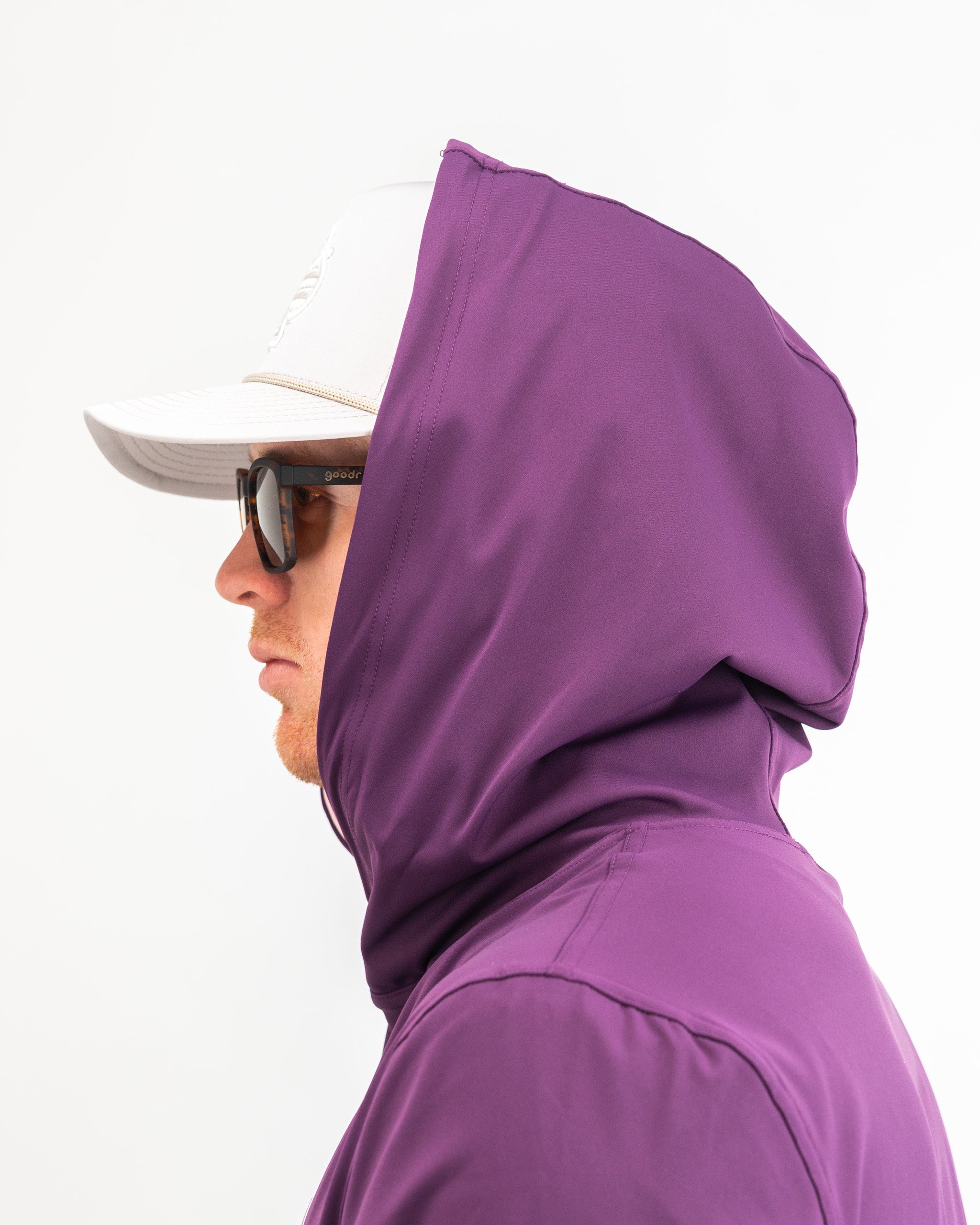 Side view of a golfer wearing a houndstooth raspberry performance hoodie, showcasing its stylish design and hood.